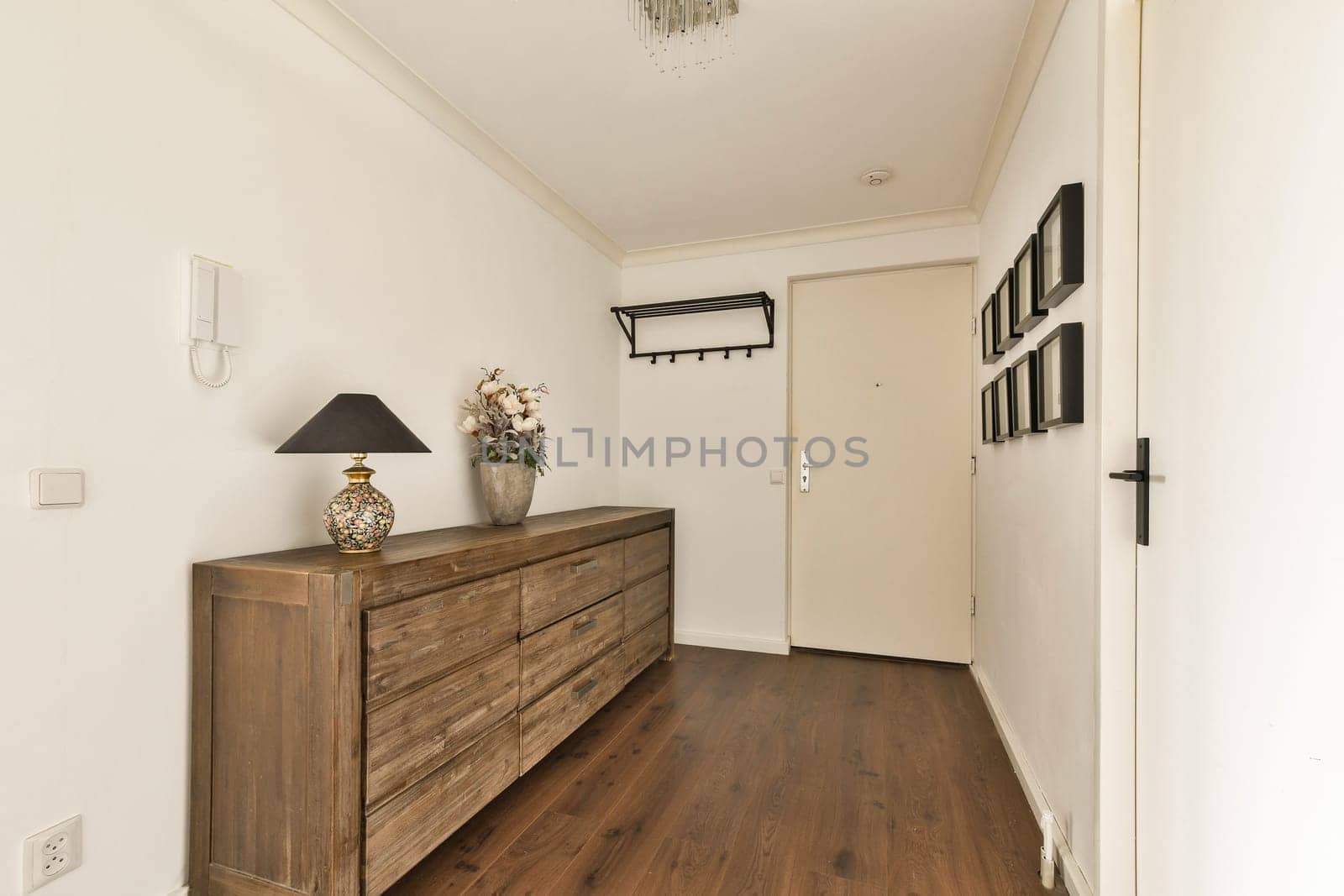 A stylish, modern hallway featuring a wooden storage unit, lamp, and decorative items, creating an inviting atmosphere.