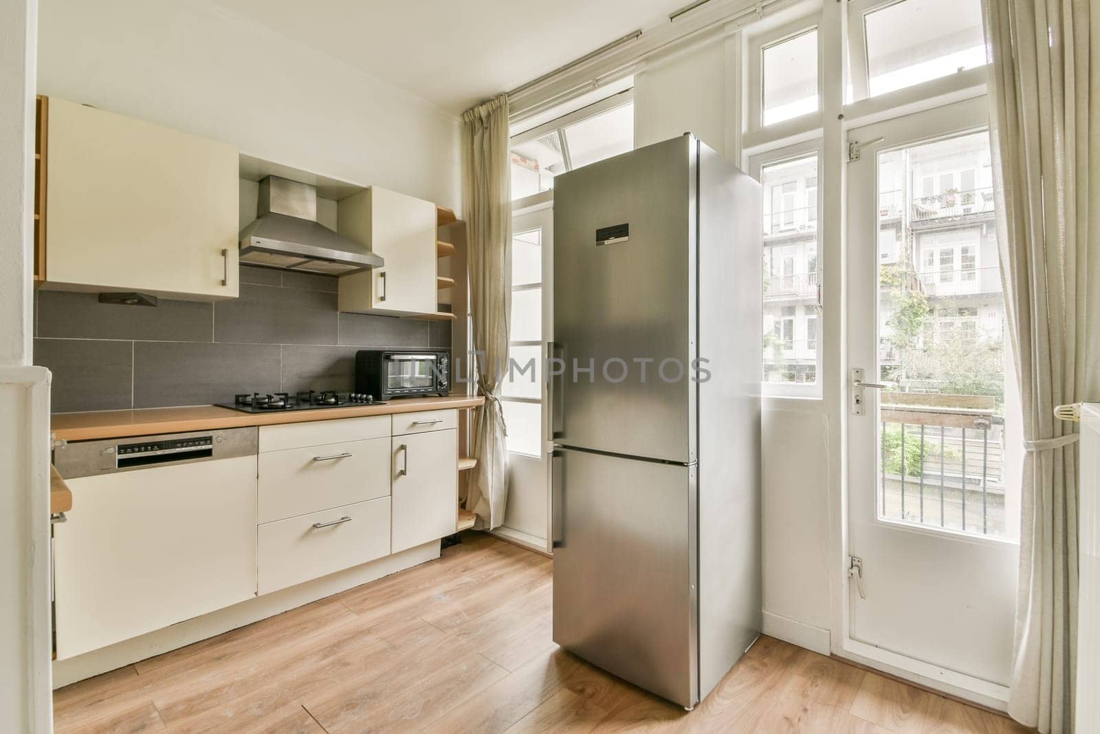 A sleek, modern kitchen featuring a stainless steel refrigerator, minimalist cabinetry, and large windows allowing ample natural light. Ideal for contemporary living.