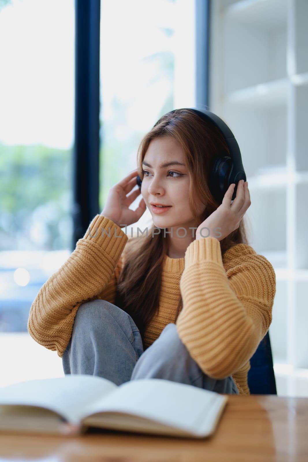 Young woman enjoying a relaxing music break at her desk while using headphones, writing in a notebook, and working on her laptop for calm inspiration.