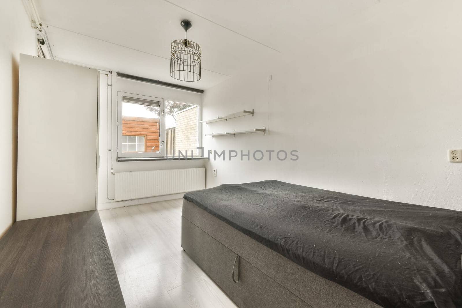 A stylish minimalist bedroom featuring a single bed, modern light fixture, and large window, creating a serene atmosphere for relaxation.