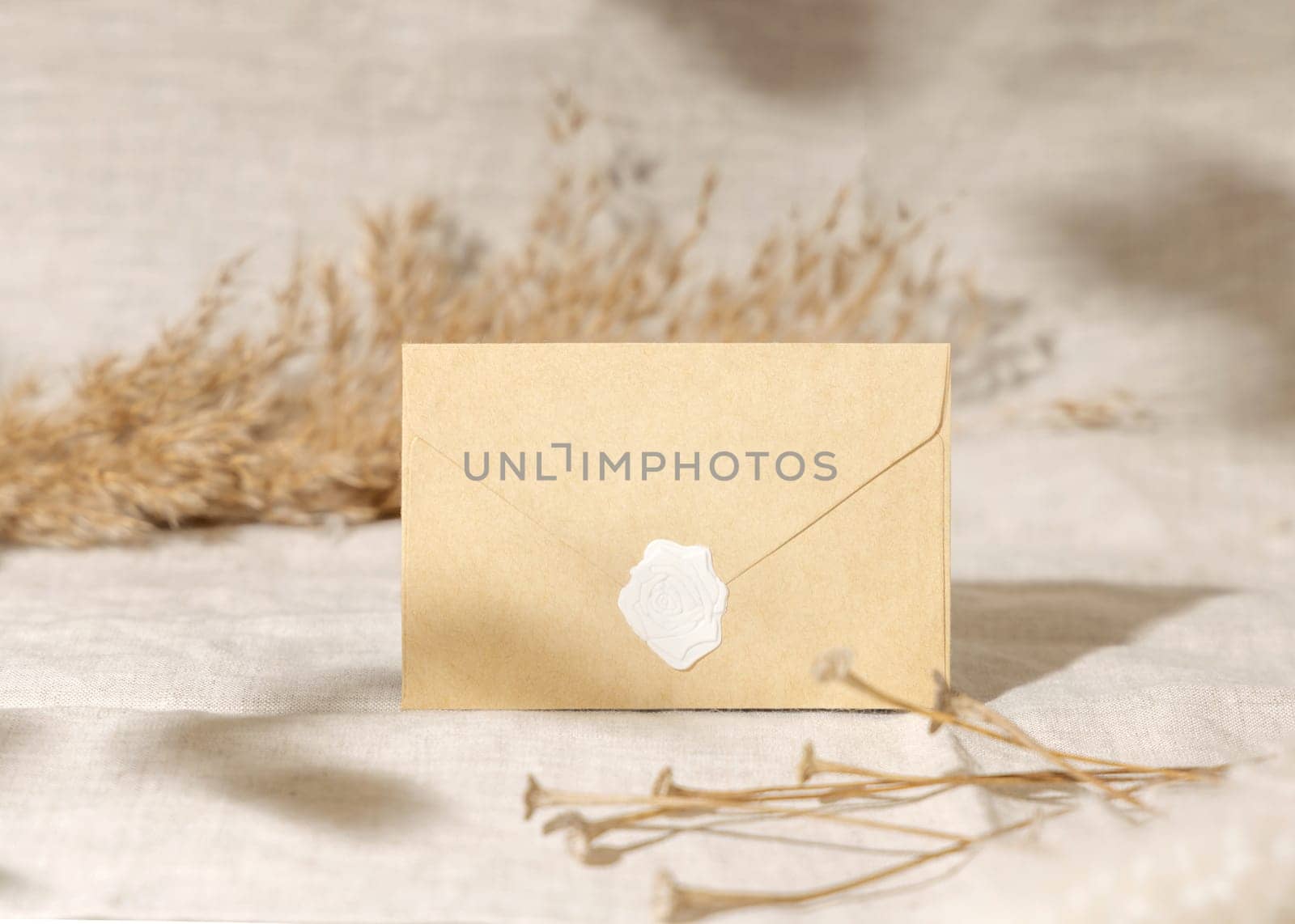 Sealed envelope against dry beige pampas grass on linen closeup, mockup. Boho scene with blank envelope, Bohemian or close to nature wedding stationery and party design. Minimal composition