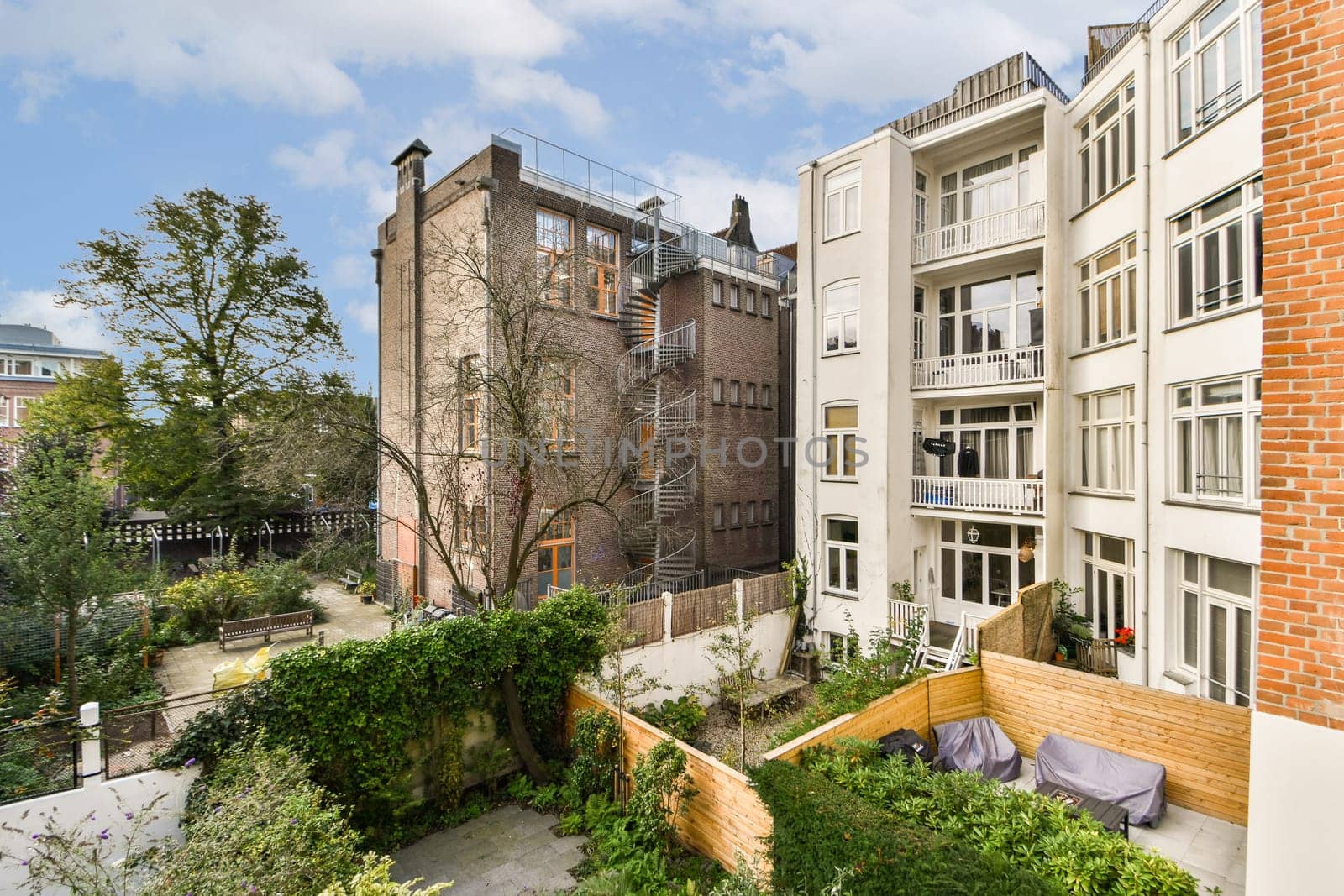 A contemporary apartment building facade juxtaposed with a lush garden and a brick structure, showcasing urban life and nature's harmony.