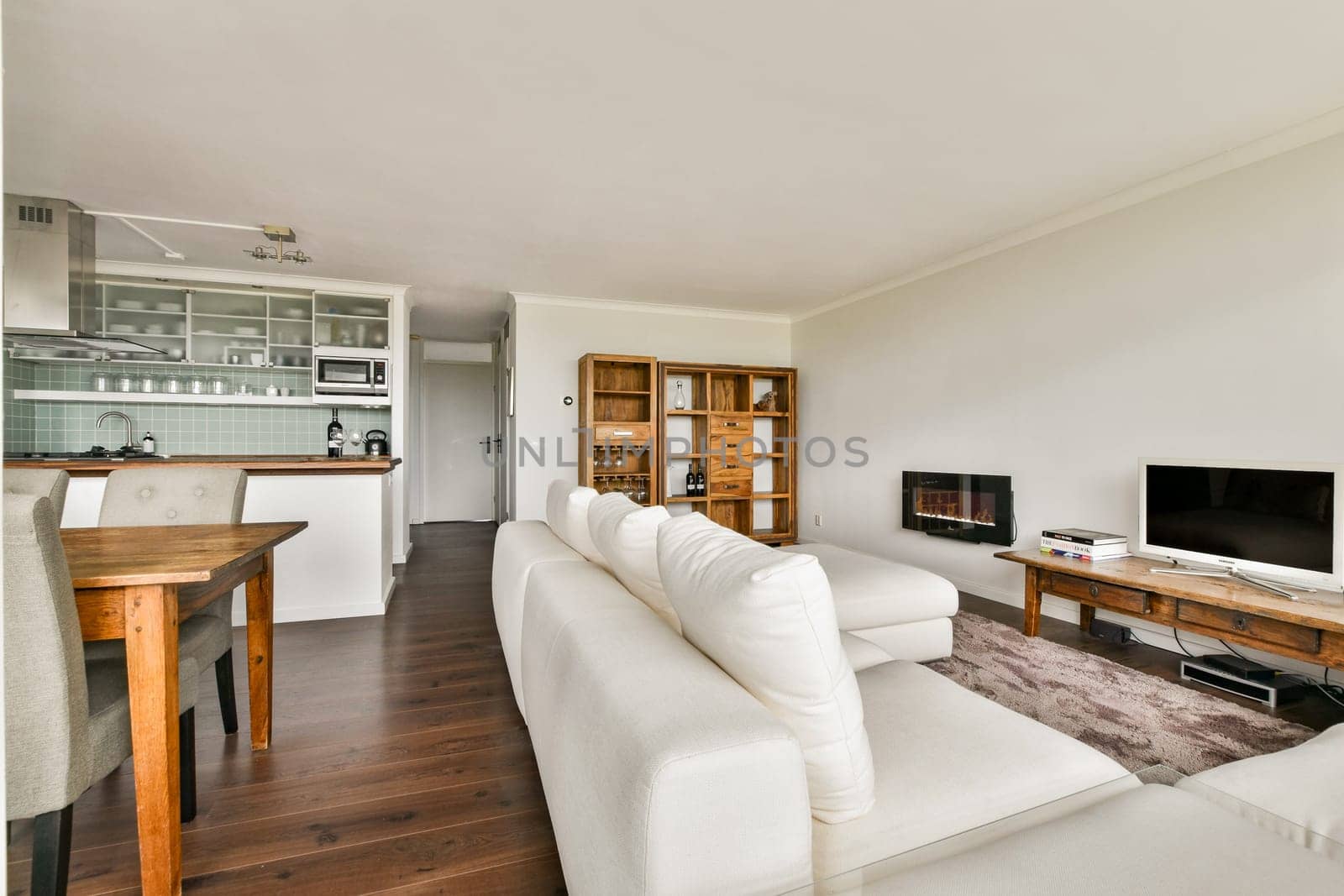 A stylish and modern living room featuring a wooden dining table, elegant furniture, and a sleek television setup in a bright minimalist space.
