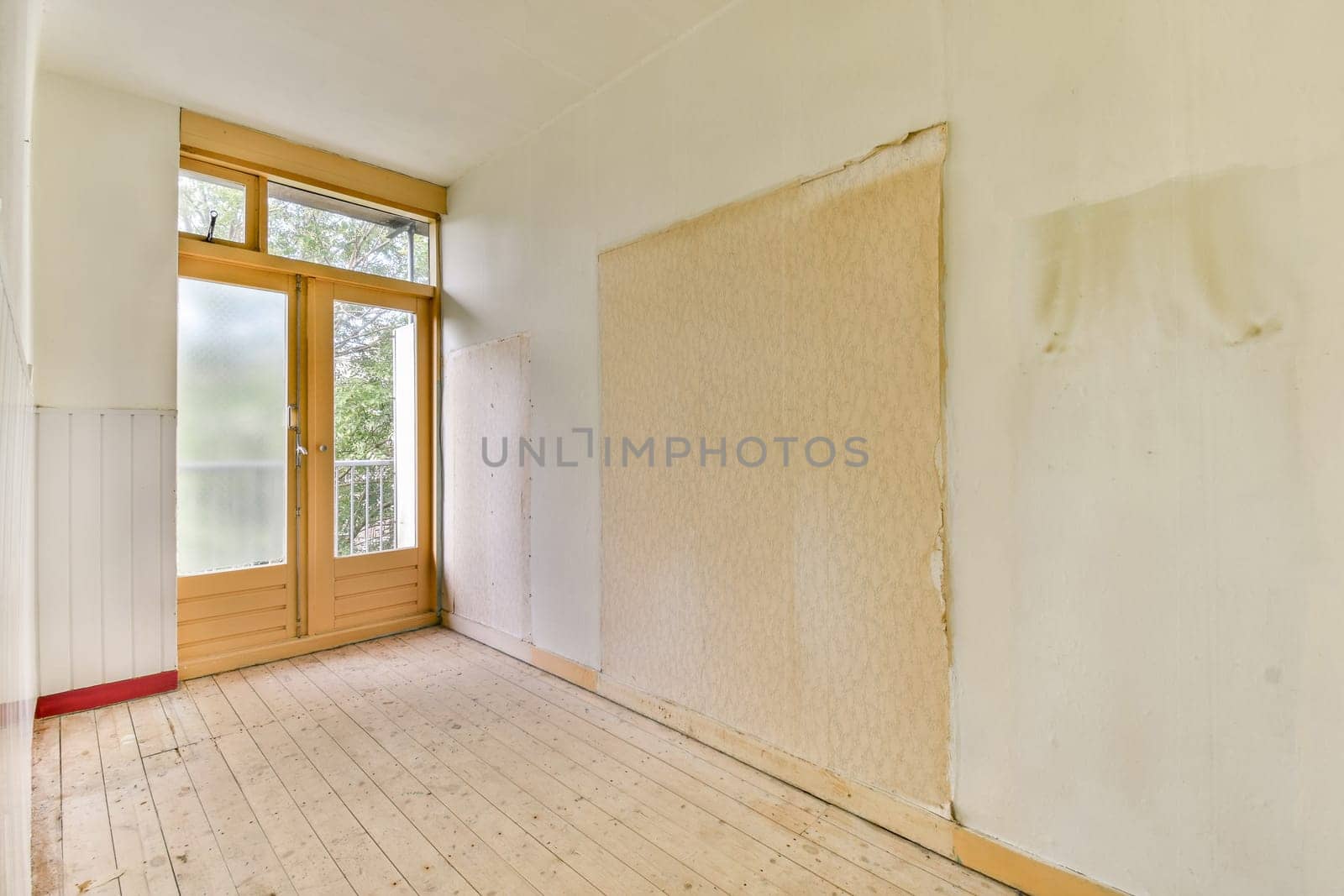 A vacant room featuring pale walls and a large window that allows natural light to fill the space. The floor is wooden, enhancing the minimalist aesthetic.