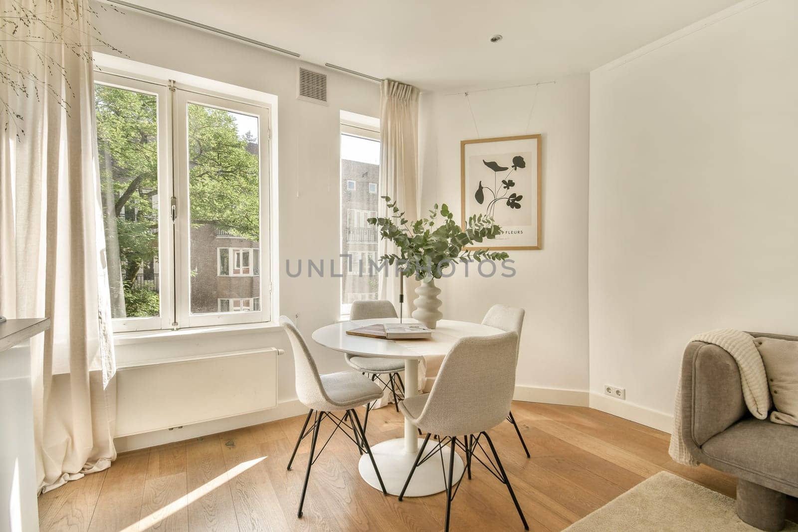 A stylish dining area featuring a round table surrounded by elegant chairs, large windows letting in natural light, and a touch of greenery.