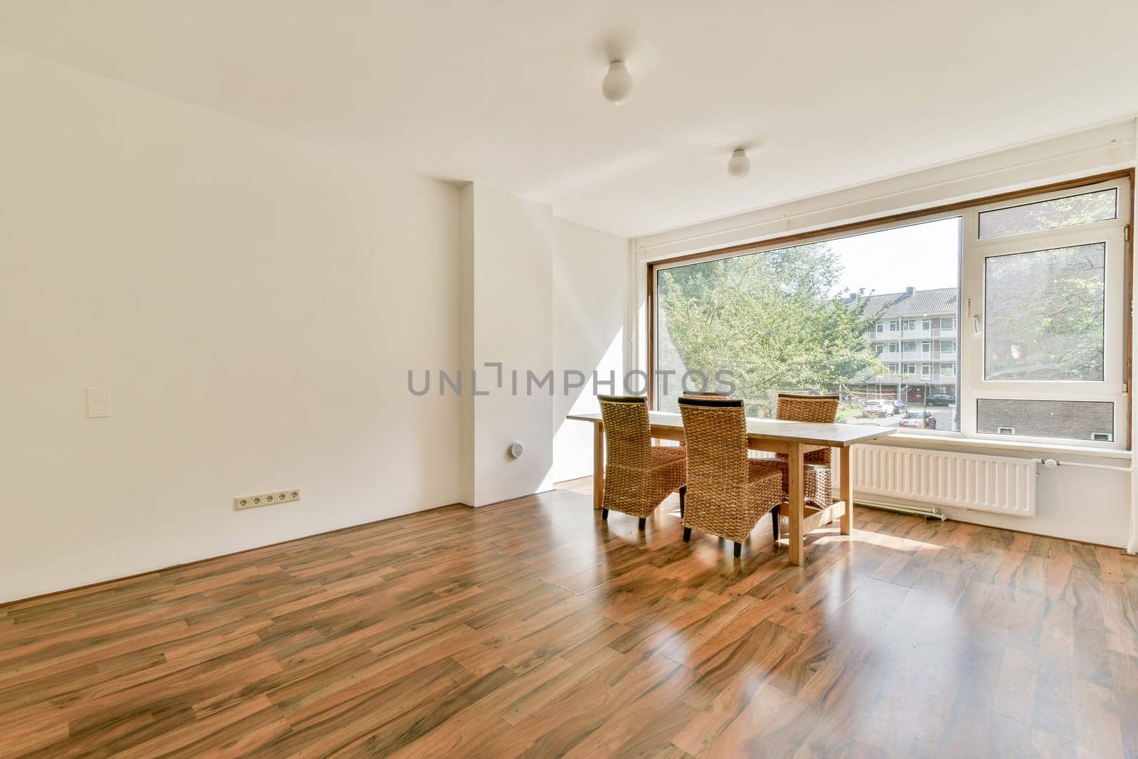 A spacious minimalistic room featuring wooden floors, natural light streaming through large windows, and a simple furniture arrangement creating a serene atmosphere.