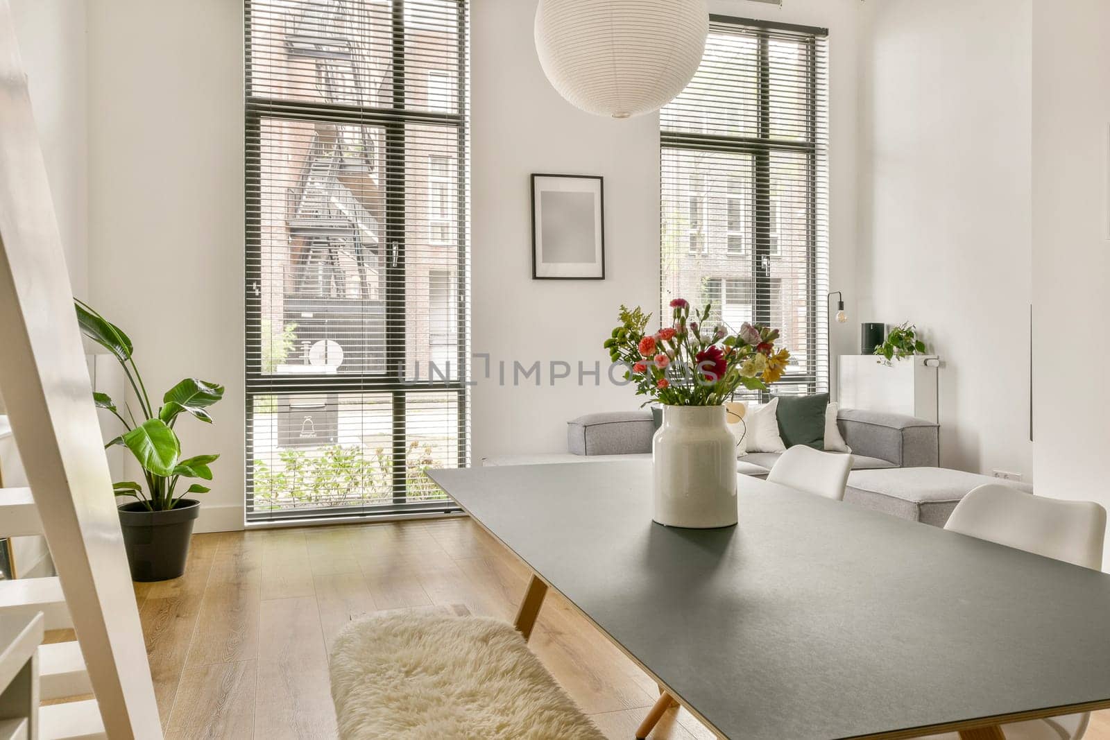 A stylish modern living space featuring natural light, a minimalist table, potted plants, and decorative flowers in a vase, highlighting comfort and elegance.