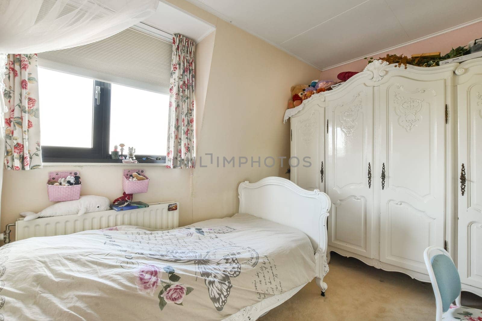 A charming bedroom showcasing a neatly made bed, classic wardrobe, and tasteful decor, illuminated by natural light from the window.