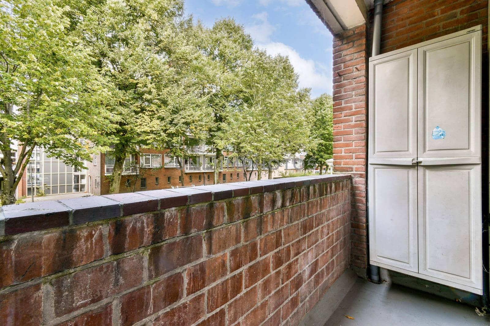 A contemporary balcony scene featuring a brick railing, greenery, and urban architecture in the background creating a vibrant living space.