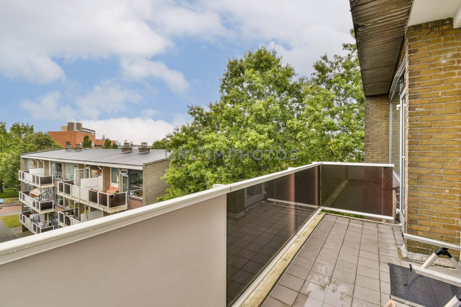 Spacious balcony overlooking lush greenery and modern architecture, featuring glass railing and stone flooring. An inviting outdoor space for relaxation.