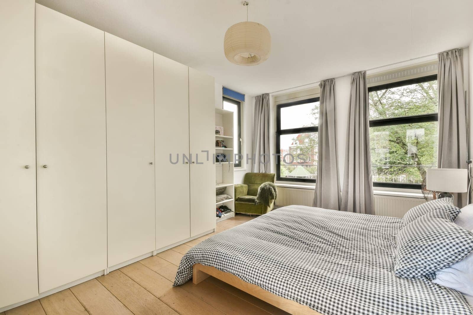 A contemporary bedroom featuring a neatly made bed, large windows allowing natural light, and stylish furniture. The minimalist design enhances comfort and relaxation.