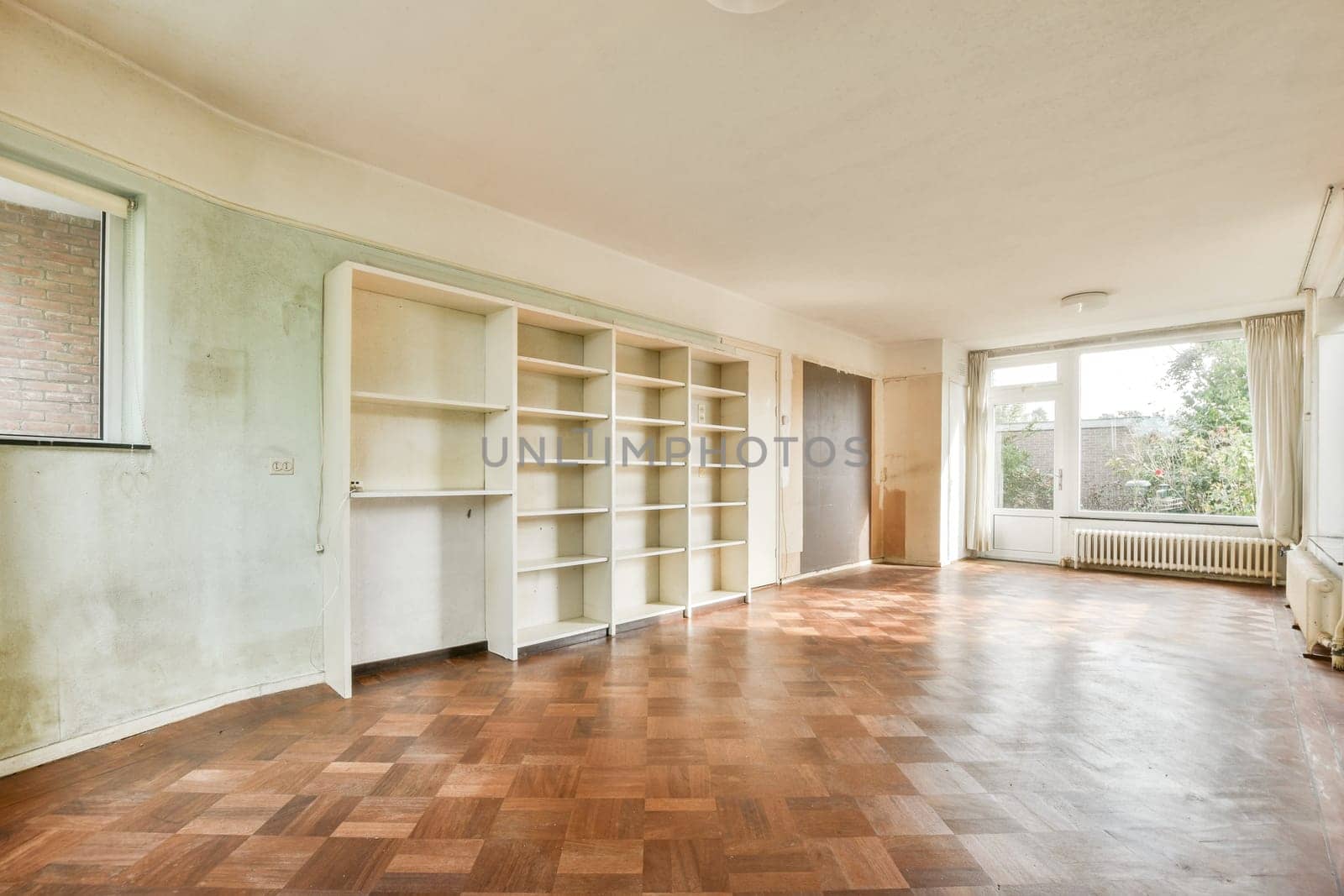 A vacant room featuring large windows that allow natural light to flood in, highlighting the wooden floor and white walls. Perfect for renovation or new decor.