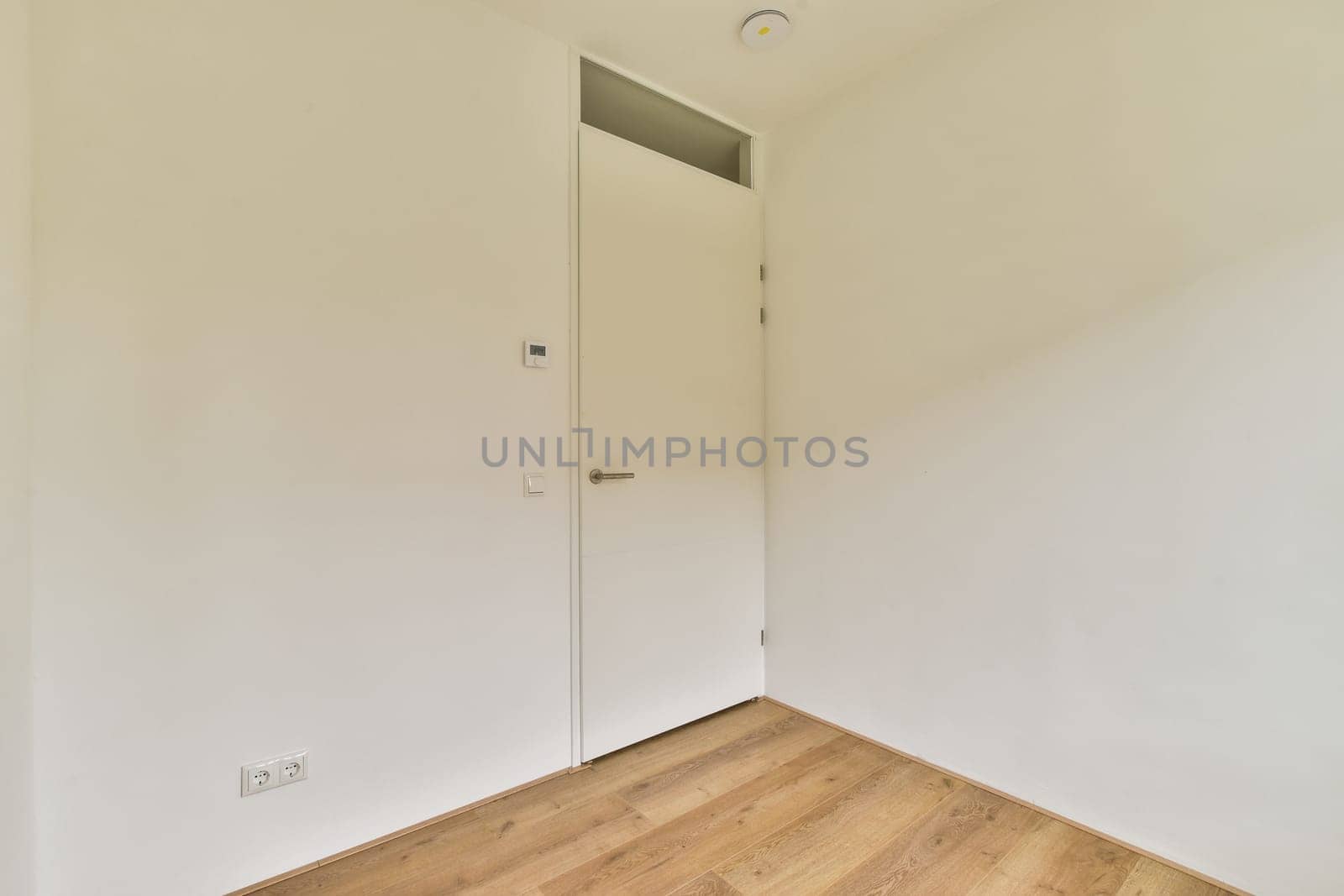 A minimalist interior space featuring a white door and light wood flooring, creating a clean and modern aesthetic in the room.