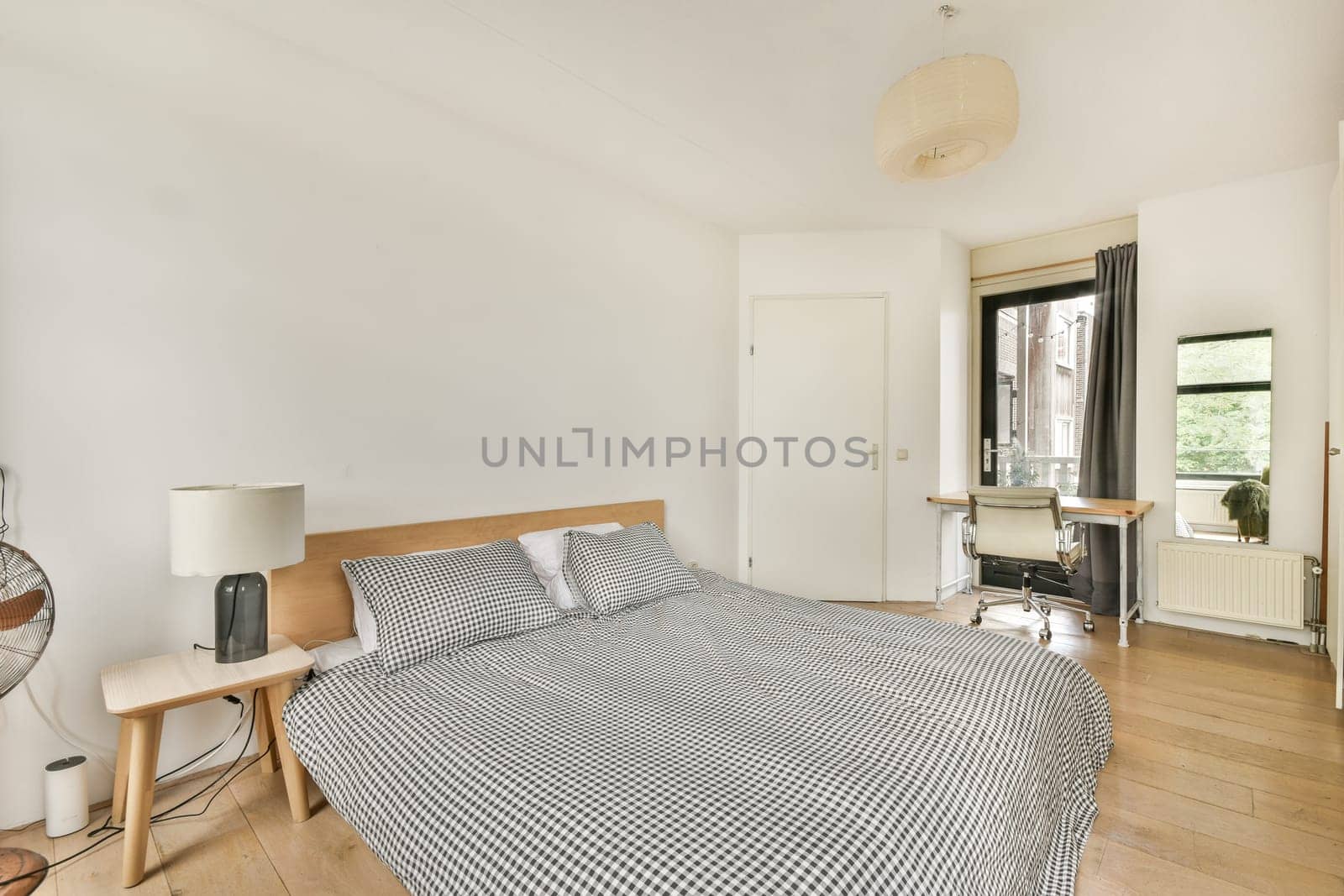 A contemporary bedroom featuring a large bed with checkered bedding, minimalist furnishings, and natural light pouring in through large windows.