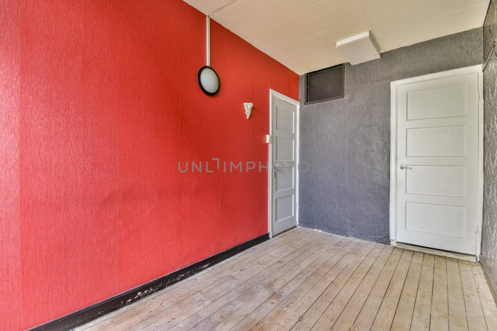 An engaging interior space featuring a striking red wall contrasted by a gray wall, creating a modern aesthetic. The wooden floor adds warmth to the design.