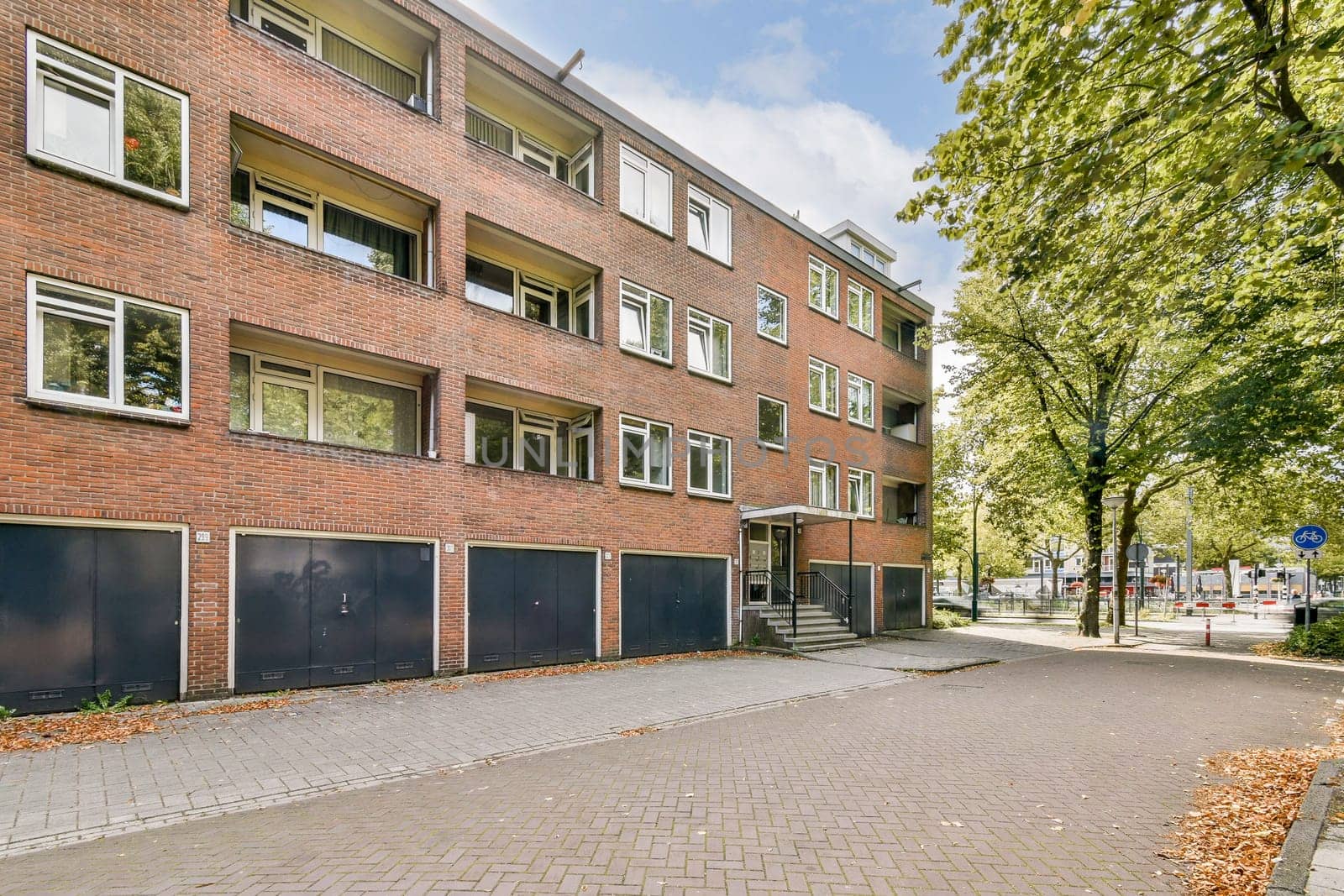A contemporary apartment complex featuring a brick exterior, positioned amidst green trees and a well-maintained pathway leading to the entrance.