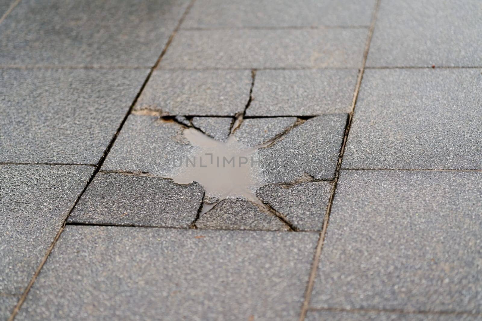 Destroyed sidewalk slab with a puddle of rainwater on a sidewalk in the city center of Swinoujscie, Swinoujscie in Poland