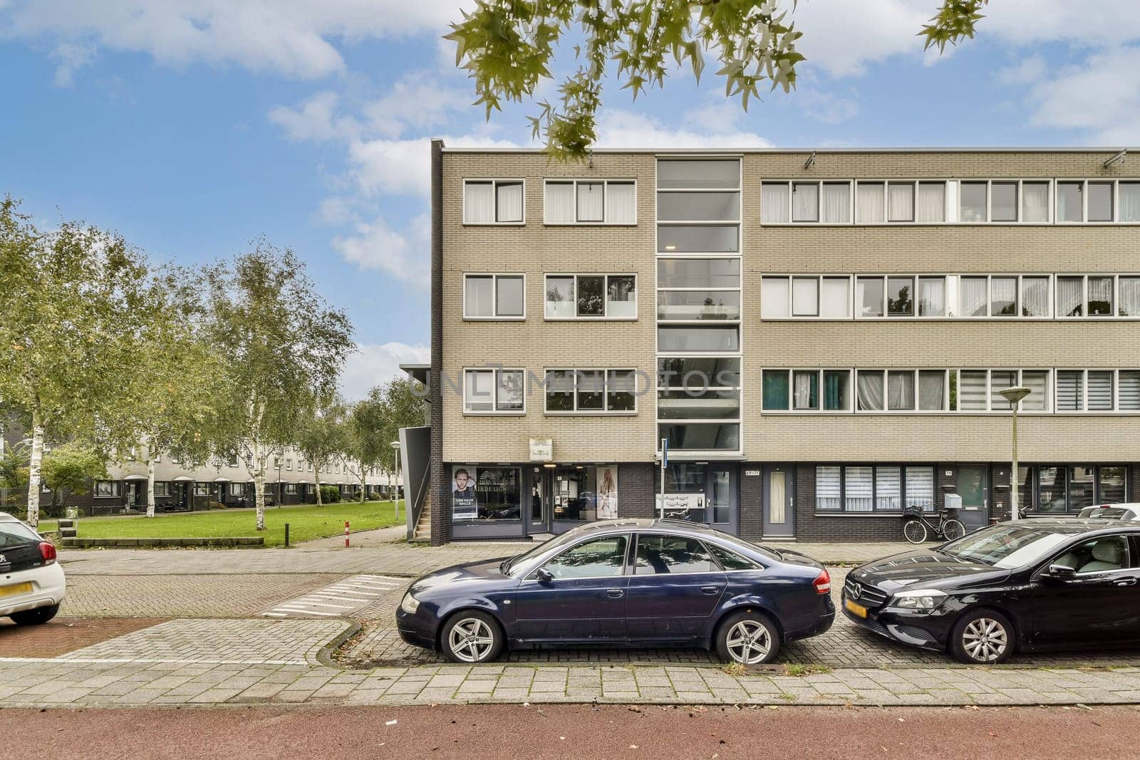 A modern multi-story building features large windows, surrounded by trees and parked vehicles. The scene depicts urban architecture and transportation.