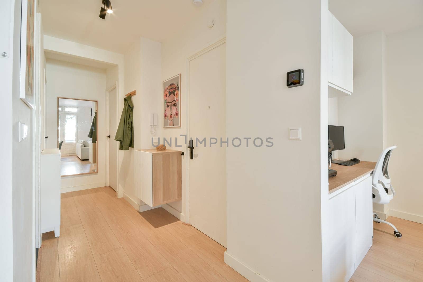 A stylish and minimalist hallway featuring a workspace with a chair, a decorative mirror, and warm wooden flooring, creating an inviting atmosphere.