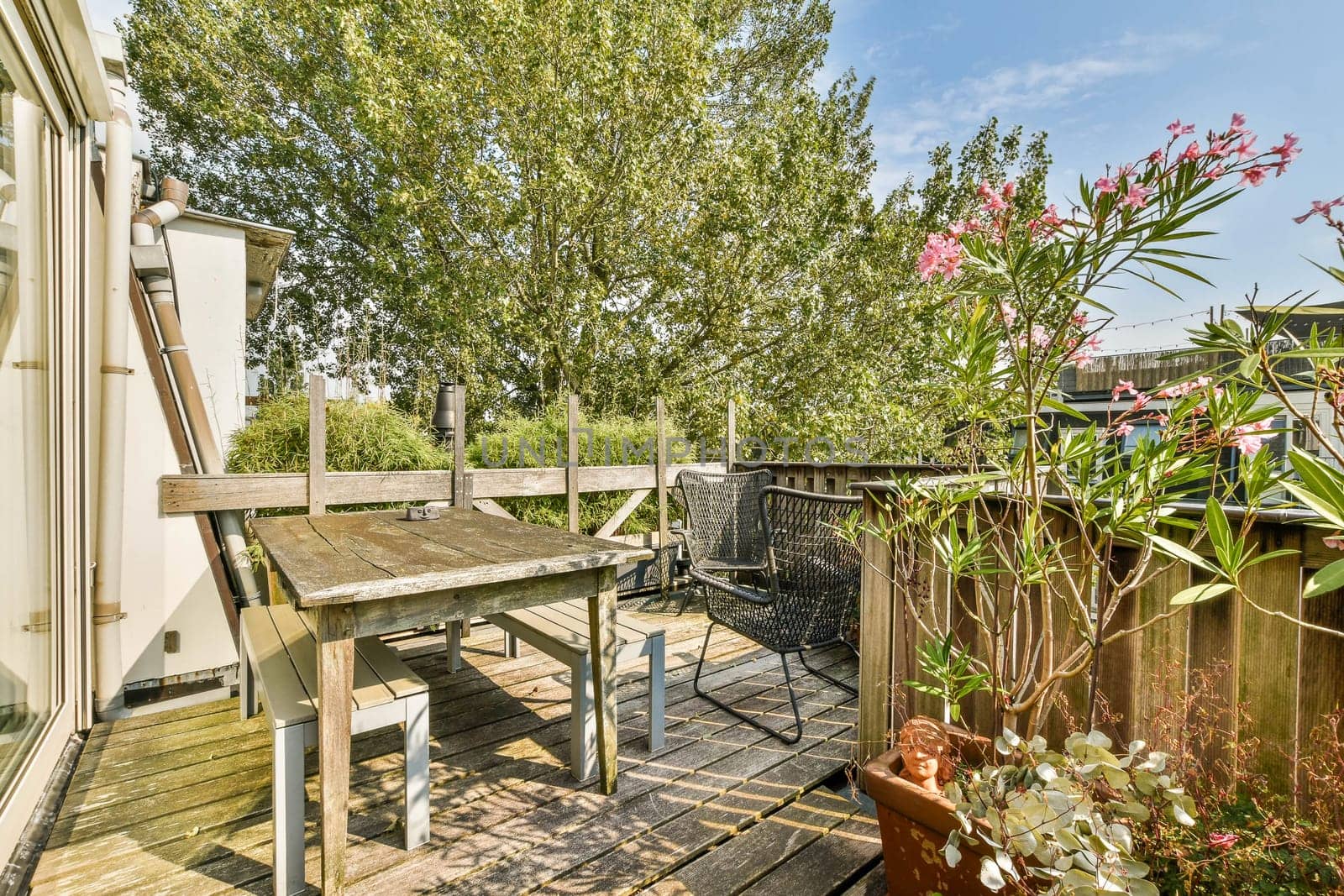 A serene outdoor patio featuring wooden furniture surrounded by lush greenery and vibrant flowers, perfect for relaxation and gatherings.
