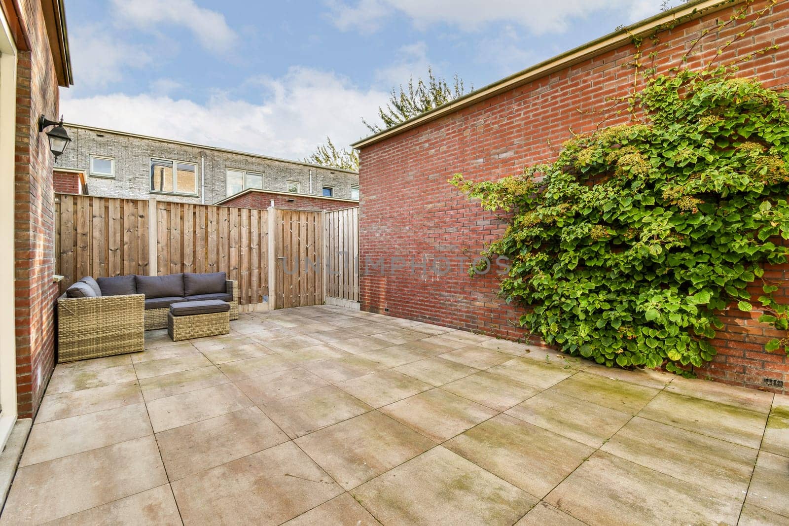 A serene outdoor patio featuring elegant seating, a brick wall backdrop, and lush greenery, perfect for relaxation and social gatherings.