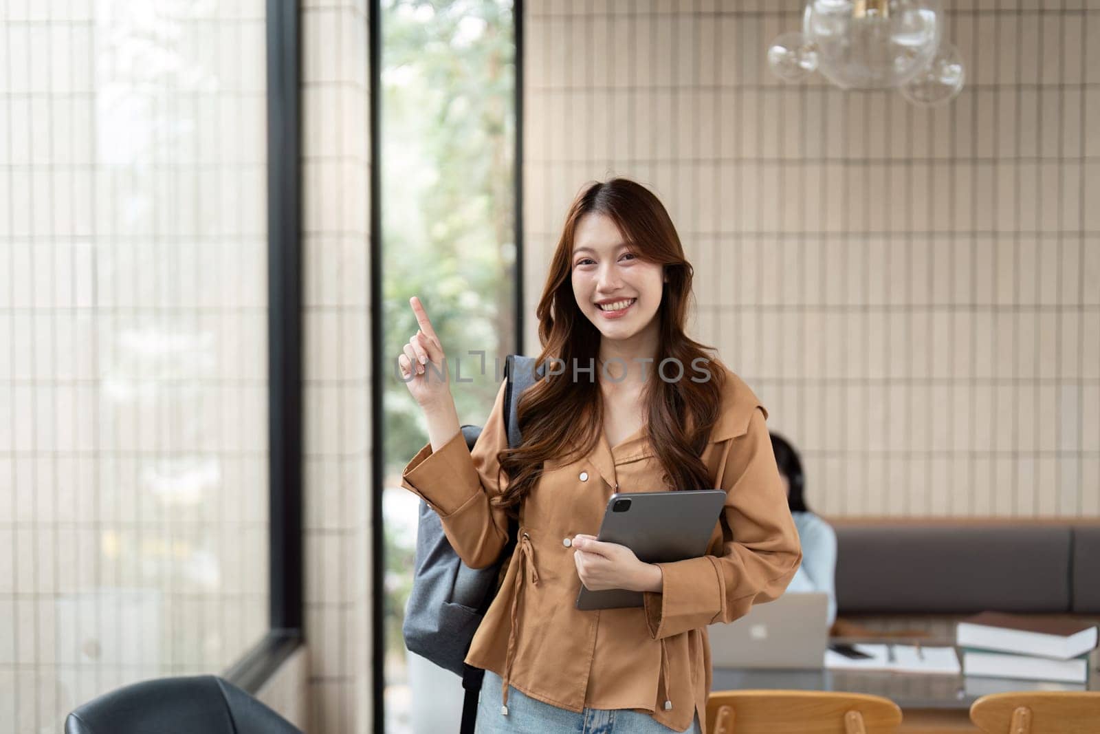 With a confident smile, a student stands with her tablet, ready to embrace new academic challenges in a trendy cafe.
