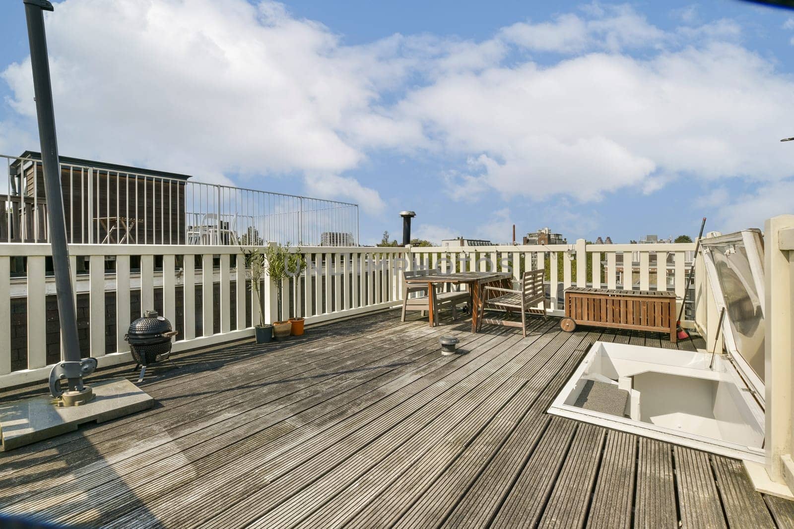 A bright rooftop terrace featuring wooden flooring, planters, and stylish furniture, ideal for relaxation and enjoying city views on a sunny day.