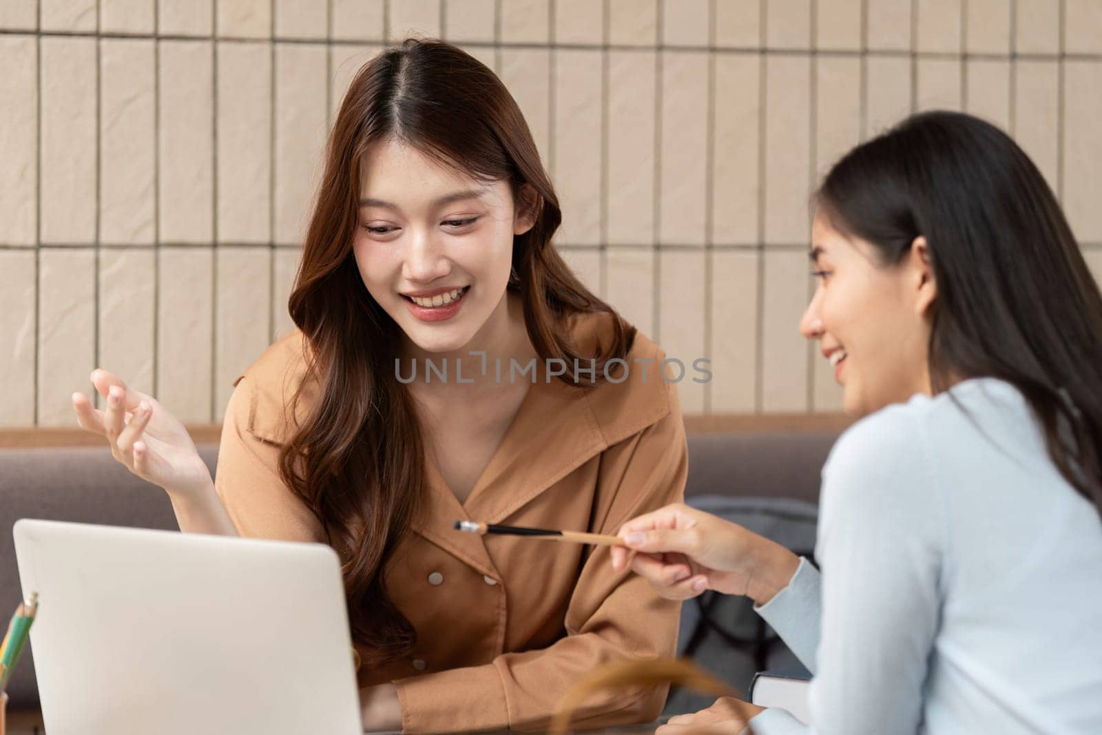 Two female students gather at a cafe, exchanging insights and focusing on their studies together, fostering collaboration and creativity in a lively setting.