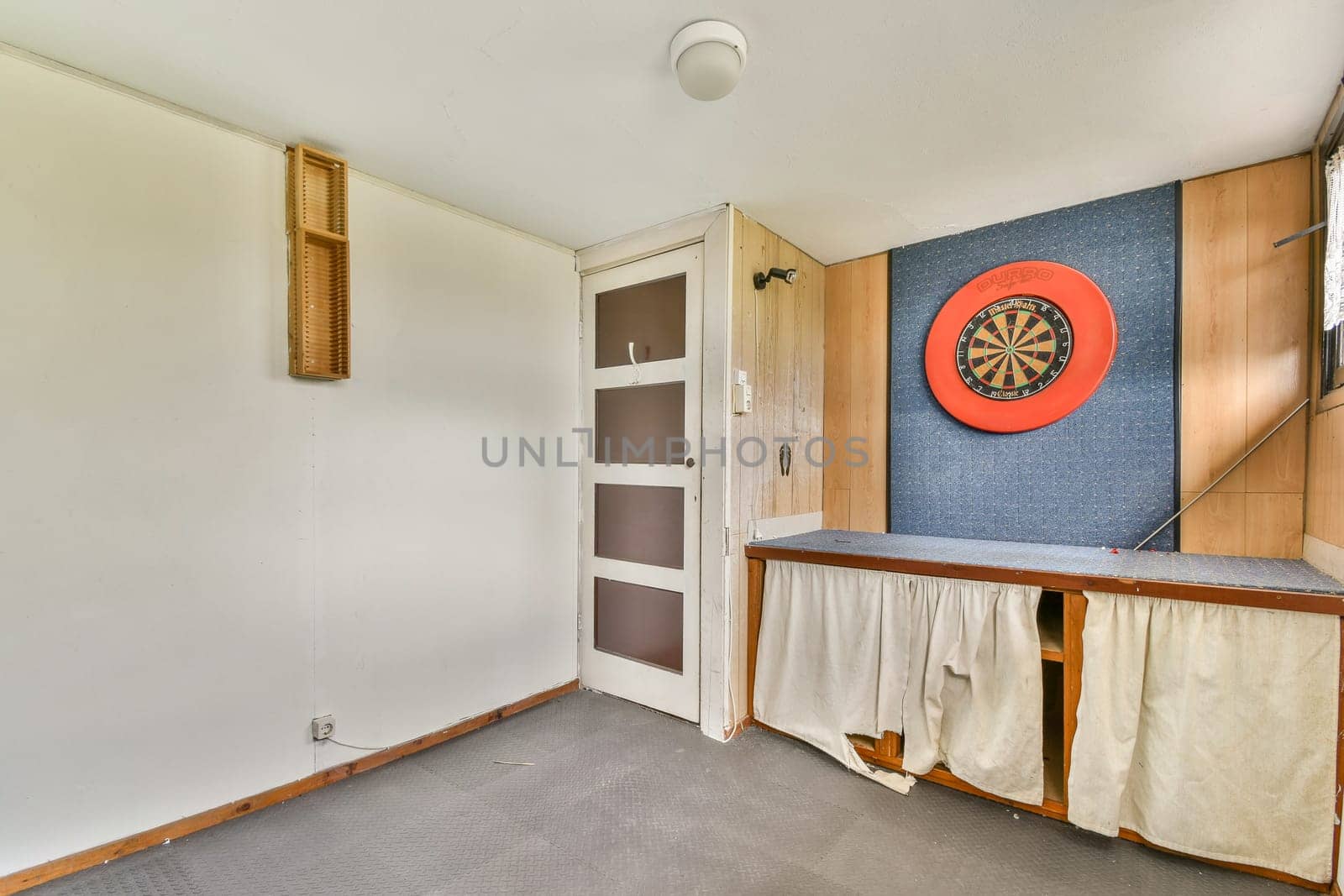 A spacious game room featuring a dartboard mounted on a blue wall, complemented by wooden furnishings and soft lighting to create an inviting atmosphere.