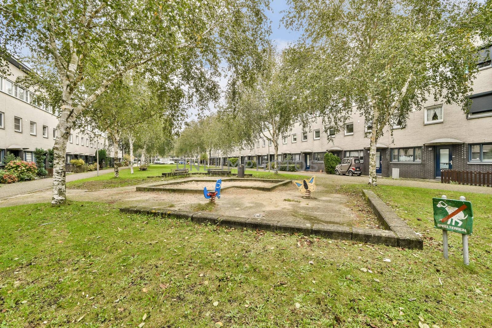 A peaceful residential neighborhood featuring green trees, a small play area, and modern buildings. Ideal for family living in an urban setting.