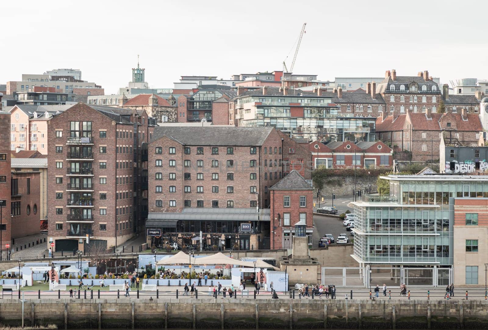 Newcastle, UK - Apr 11, 2025 - Old buildings on the Quayside area and people on the tyneside view from Sage Gateshead (The Glasshouse International Centre for Music) at Newcastle upon Tyne. use it as your Wallpaper, Poster and Space for text, Selective focus