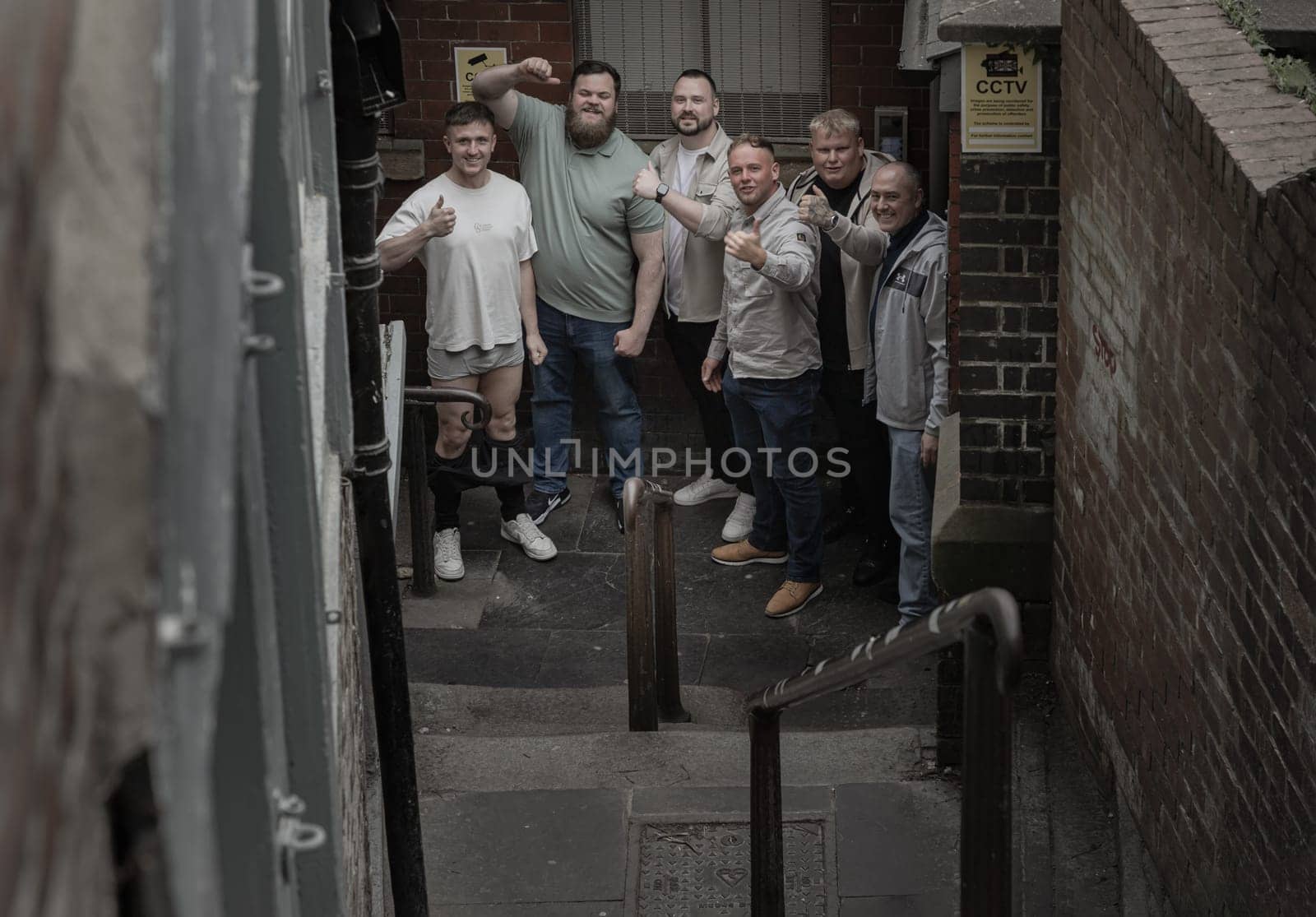 Newcastle, UK - Apr 12, 2025 - Group of cheerful male friends gathered with thumbs up emotionally and smiling posing for a portrait on the stairs leading down a narrow alley. Positive and Friendly expression, use it as your Wallpaper, Poster and Space for text, Selective focus.