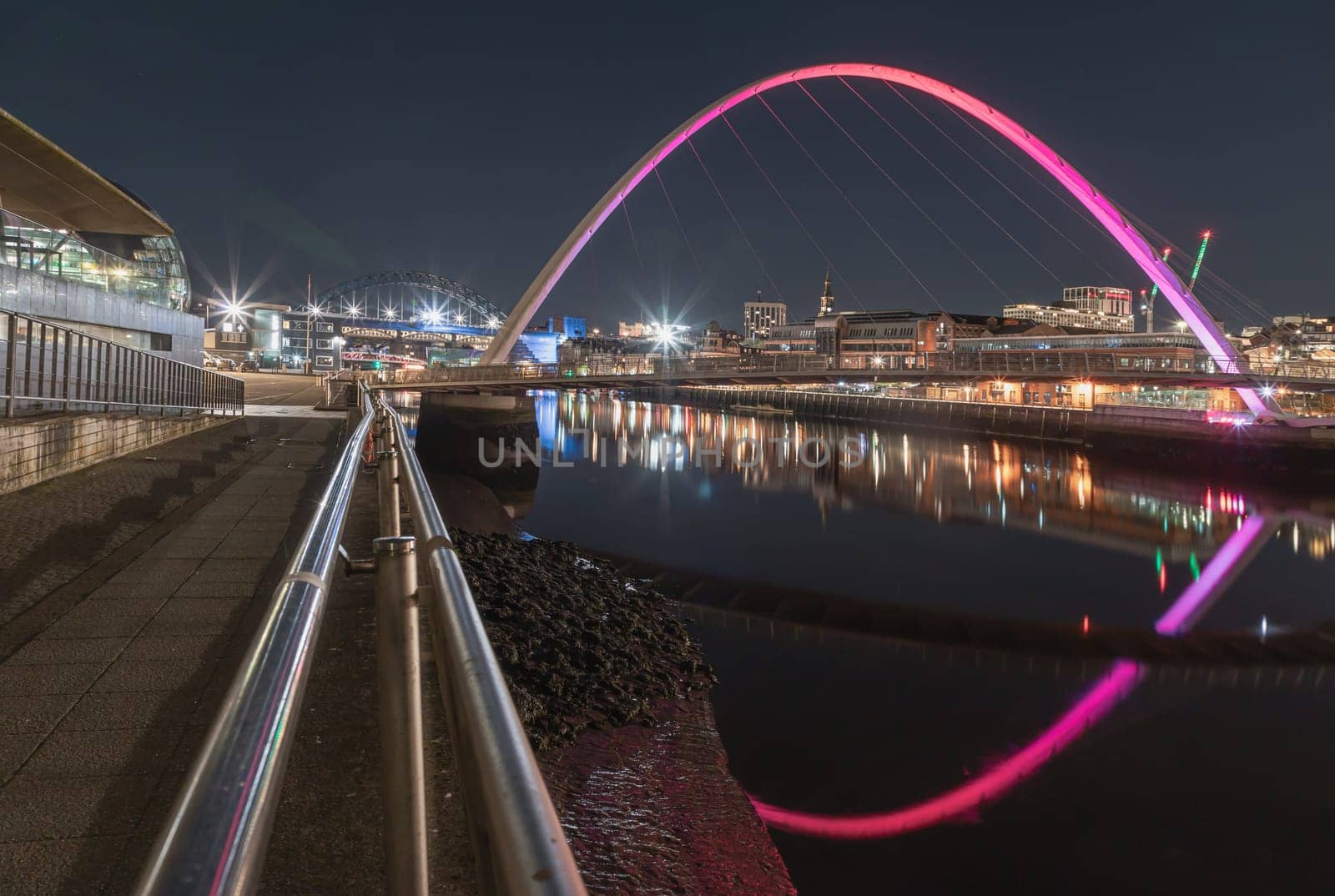 Newcastle, UK - Apr 13, 2025 - Nightscape view of The Iconic gateshead millennium bridge with Tyne bridge and dark sky in the background. The pedestrian bridge spanning the River tyne with reflection in river, use it as your Wallpaper, Poster and Copy space, Selective focus.