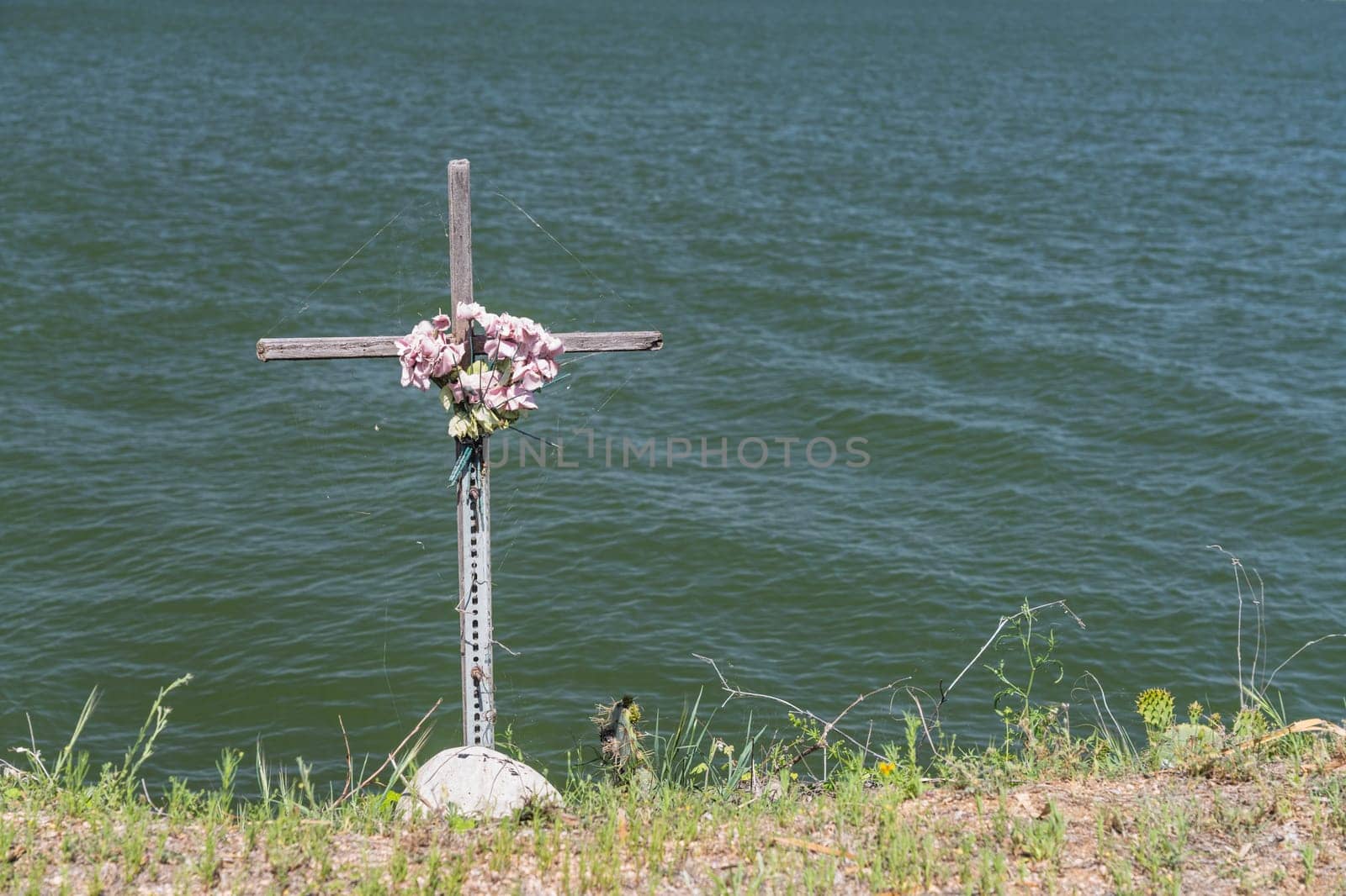 A memorial cross stands gracefully at Horseshoe Lake's edge, commemorating a life with floral tributes.