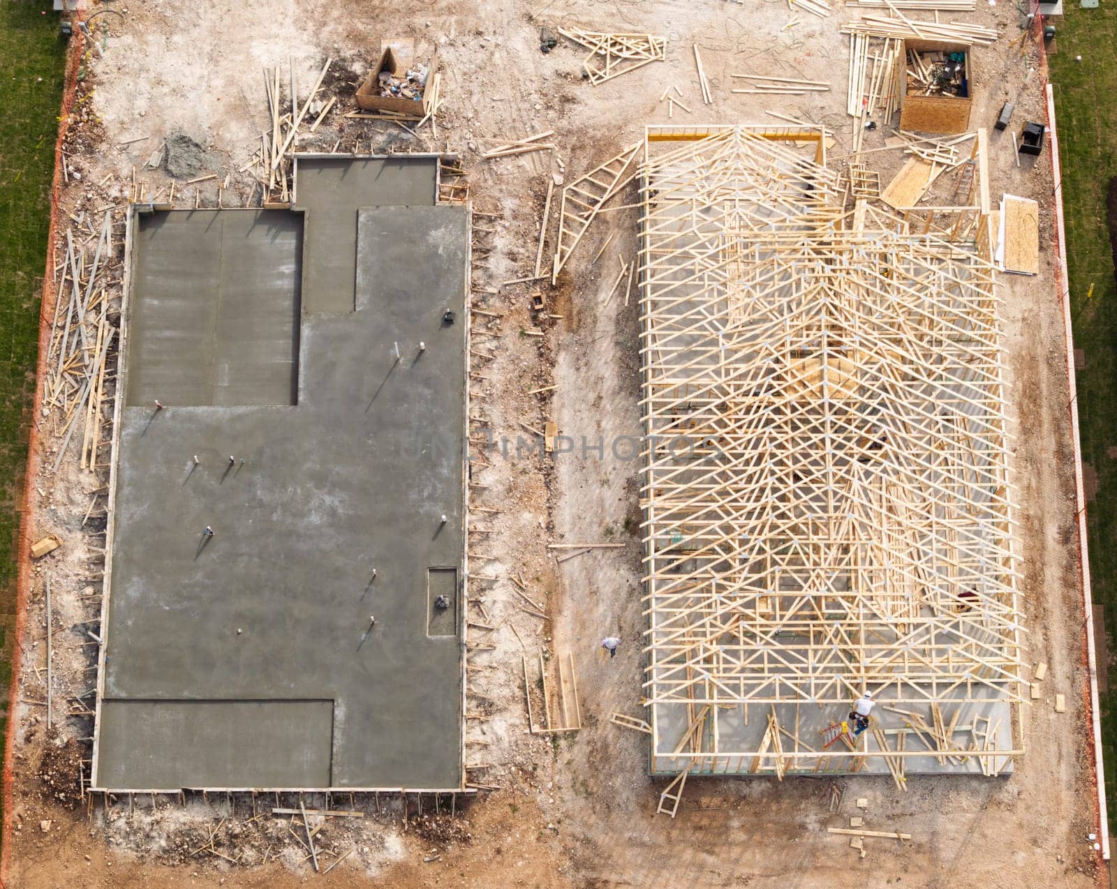 Aerial view of newly poured concrete slab next to home that is being constructed with wooden framework in Georgetown Texas
