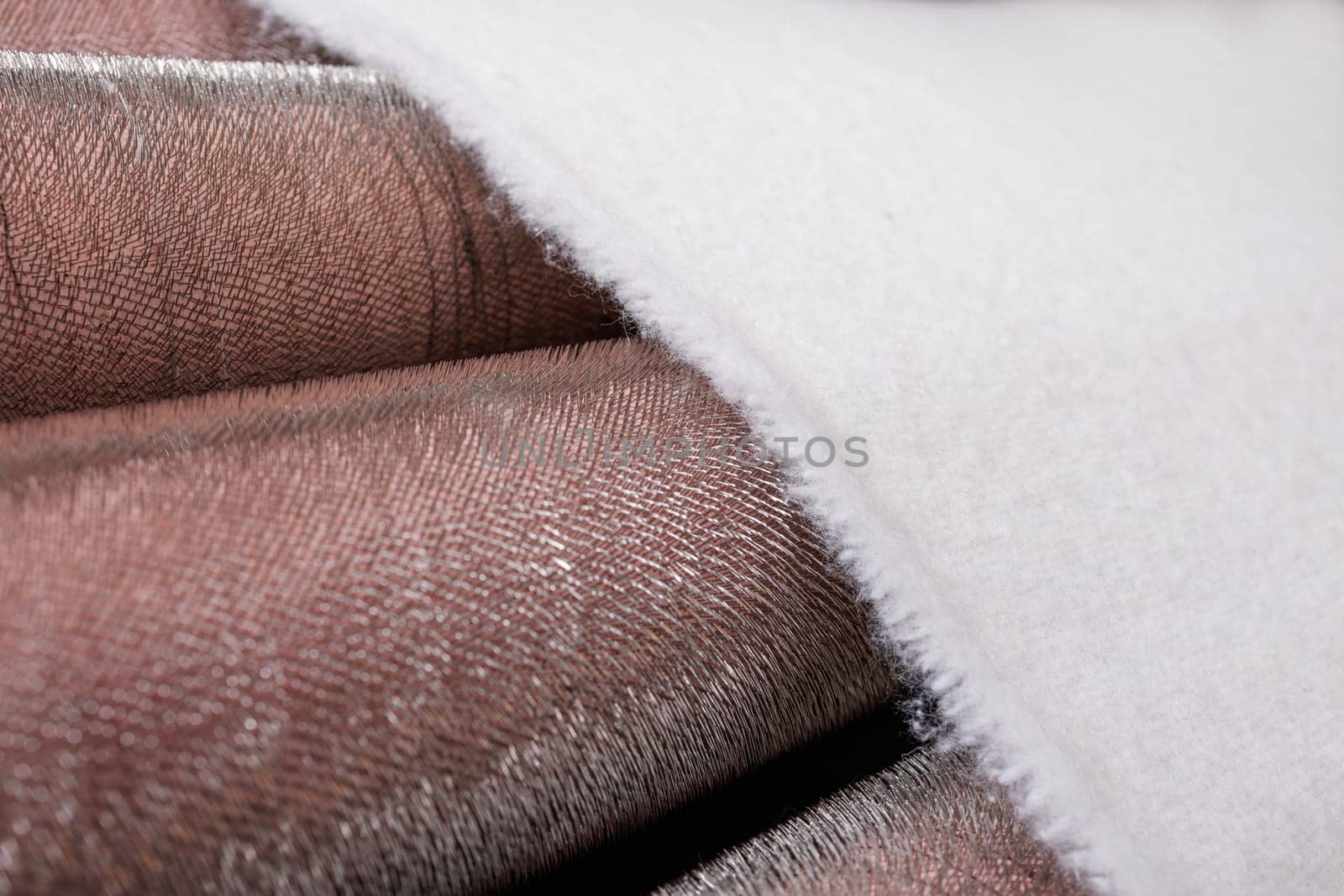 Close-up of white fabric moving through metal carding rollers during the textile manufacturing process.