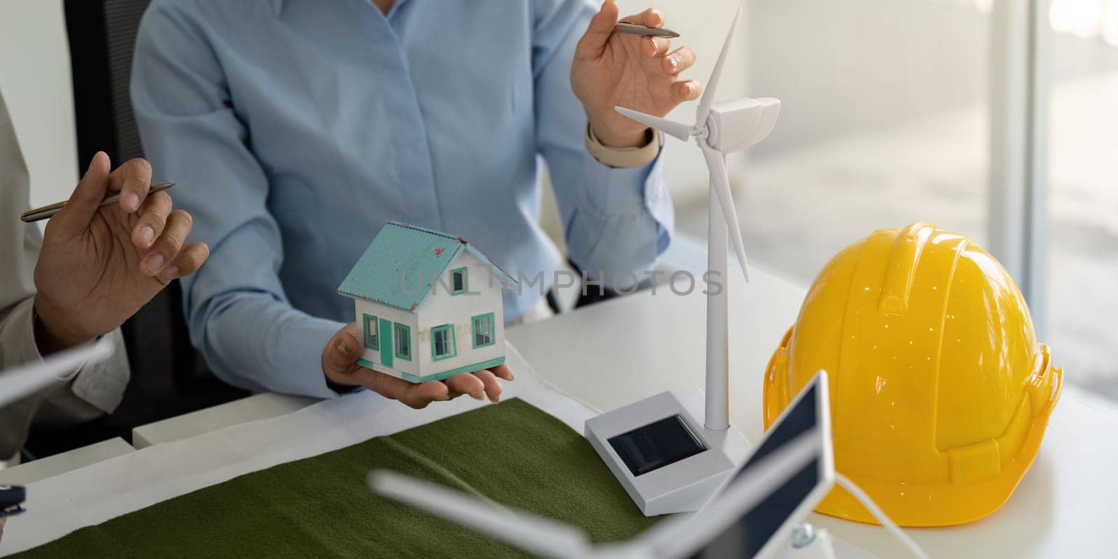 In a conference setting, professionals collaborate on sustainable construction strategies, featuring model houses and renewable energy concepts like wind turbines, emphasizing ESG principles.