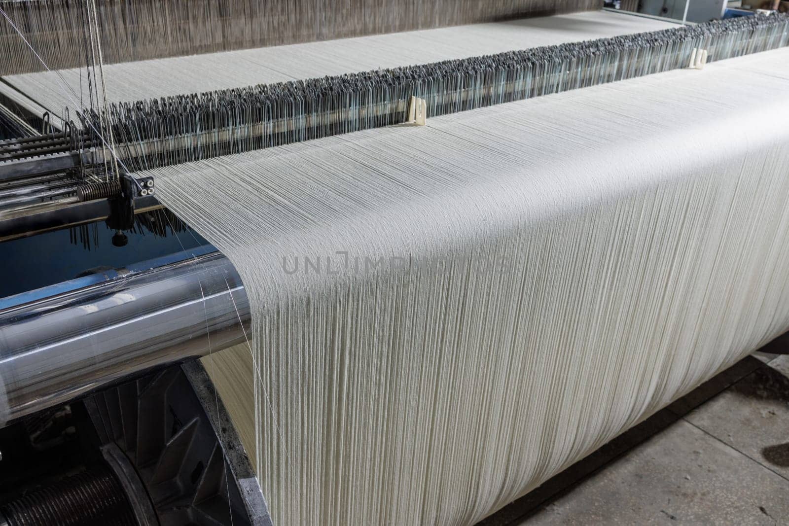 Automated textile loom weaving white yarn into fabric in a modern factory, showcasing precision threadwork.