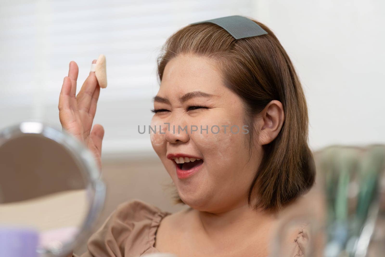 A fun-loving woman enjoys her beauty routine, playfully applying powder to her face while capturing the joy of makeup application in her cozy setting.