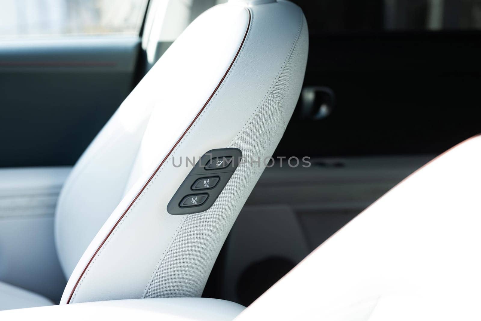 Rear seat passenger switch to control the front passenger seat. Walk-in seat switch. Luxury car interior. Electric car seat position adjustment buttons.