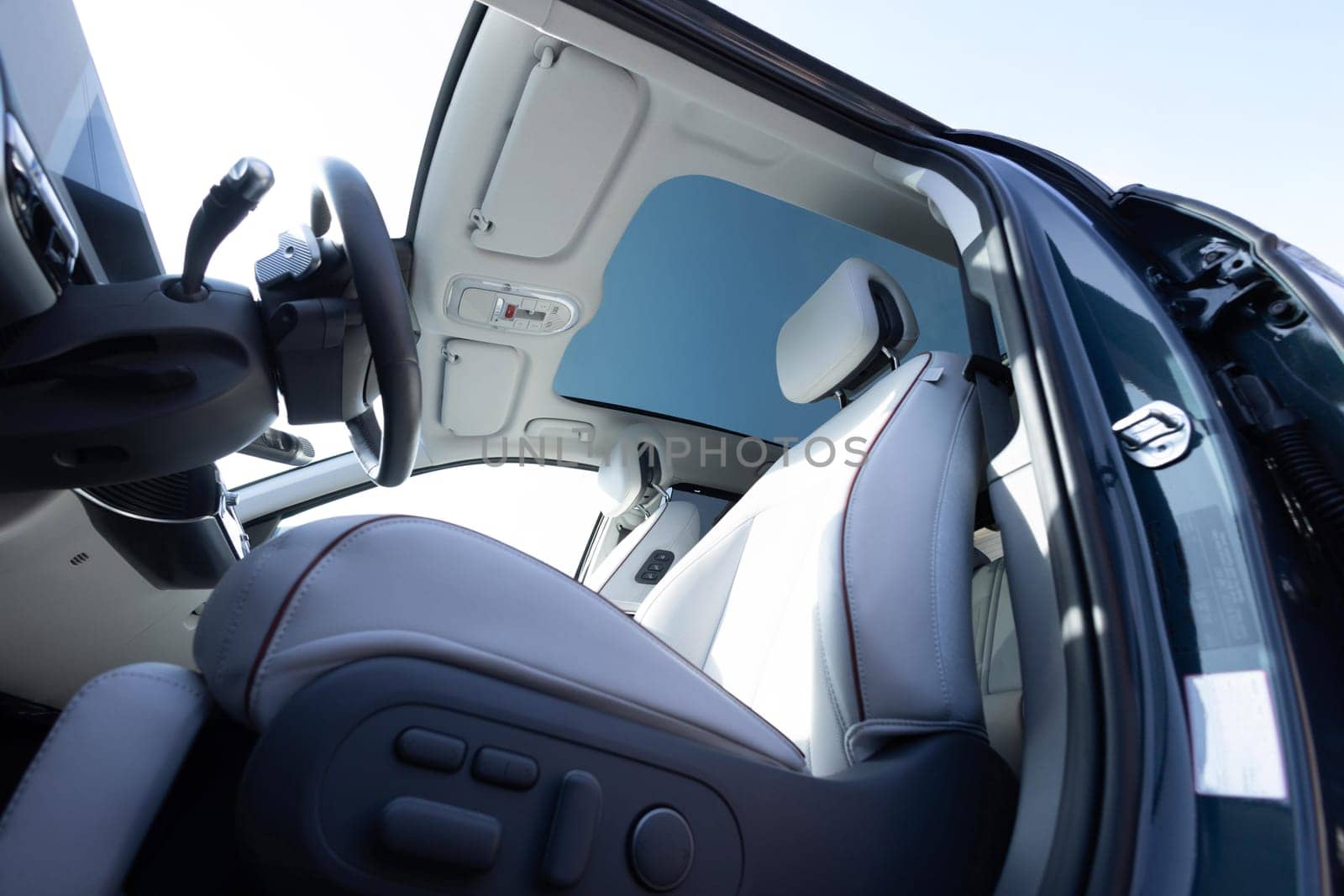 Panoramic glass sun roof in the new electric car. Clean glass and view from inside to the sky. Sunroof hatch with tinted glass. White leather interior. Modern car Interior steering wheel, shift lever.
