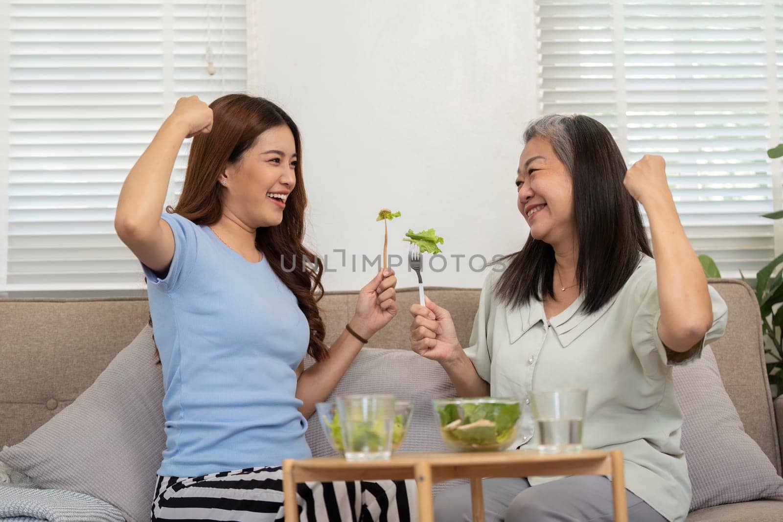 A cheerful moment shared between a mother and daughter as they celebrate their healthy choices with a playful salad cheer, representing joy and wellness.