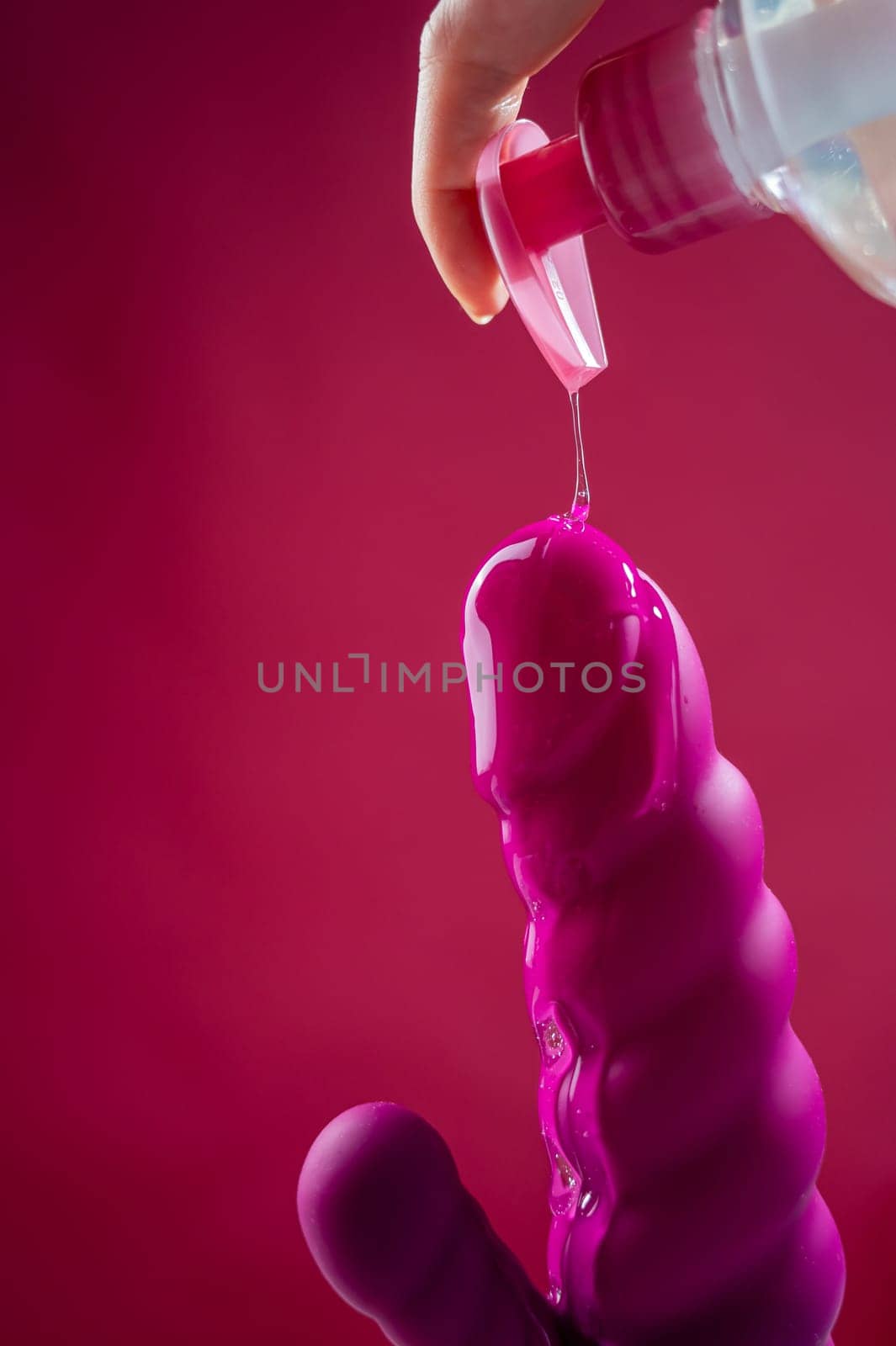 Lube pouring on pink dildo on pink background