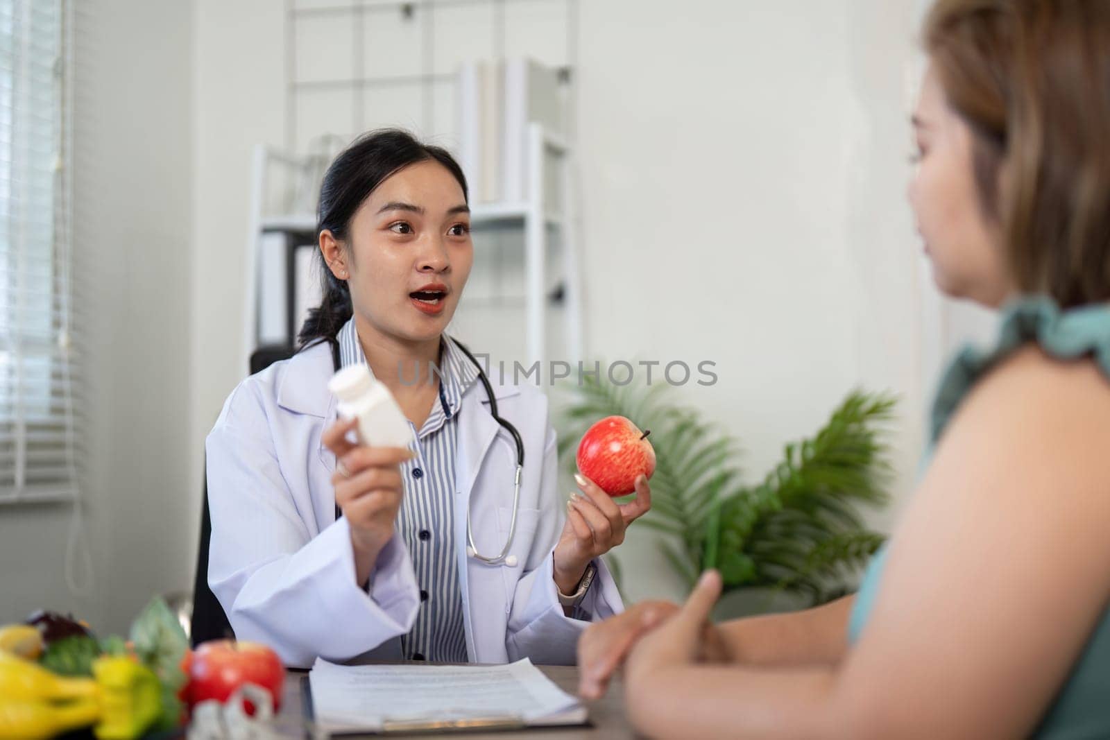 In a professional setting, a nutritionist discusses the importance of medication and healthy eating, illustrating concepts with apples and a supplement bottle.