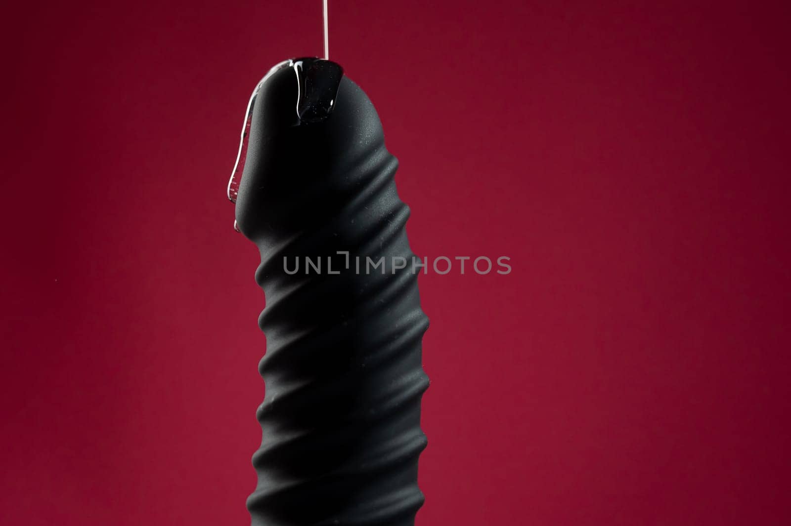 Lube pouring on black dildo on pink background