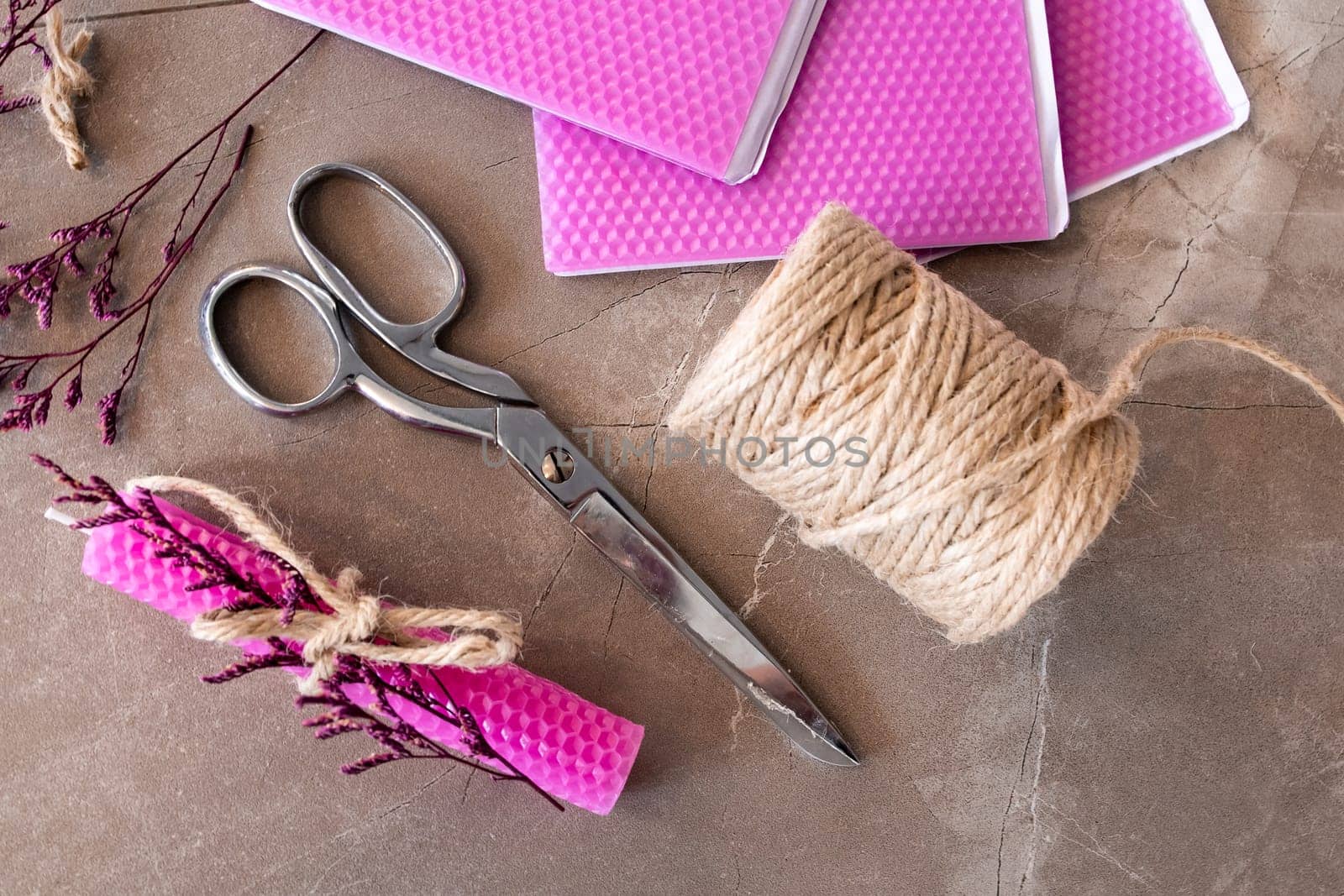Crafting materials with pink wax sheets, scissors, jute twine, and dried flowers on stone surface.