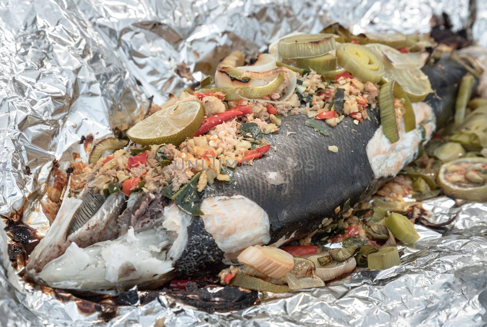 Baked Whole Salmon with Herbs in an Oven, ingredient include Coriander root, Ginger, Galangal, Kaffir lime, Leek, chopped together and Bird's eye chili with Slice lemons place on the Salmon fish. Healthy eating, use it as your Wallpaper, Poster and Space for text, Selective focus.