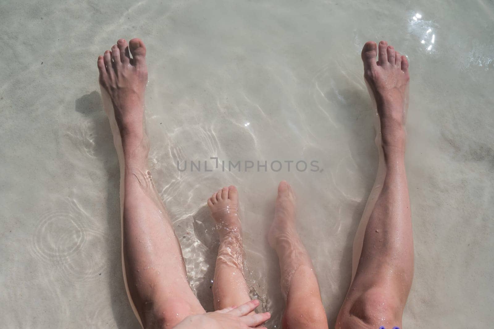 Top view of the legs of a one year old boy and his mother on the seashore
