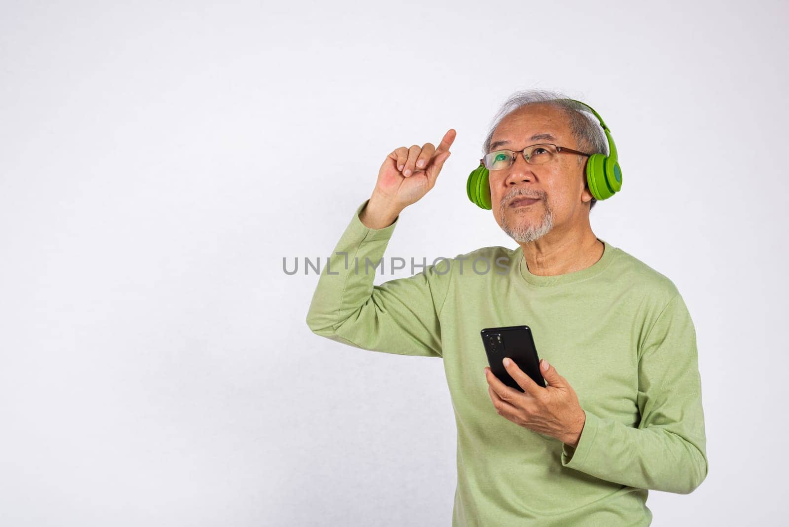 Portrait Asian smiling old man headphones is holding smartphone listen music in headphones and dancing studio shot isolated on white background, Funny senior, enjoying his music