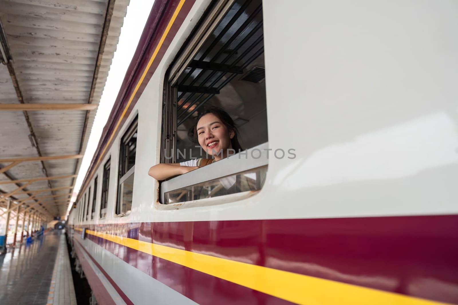 A young woman beams out of a train window, embodying the joy of travel and exploration as she takes in the sights.